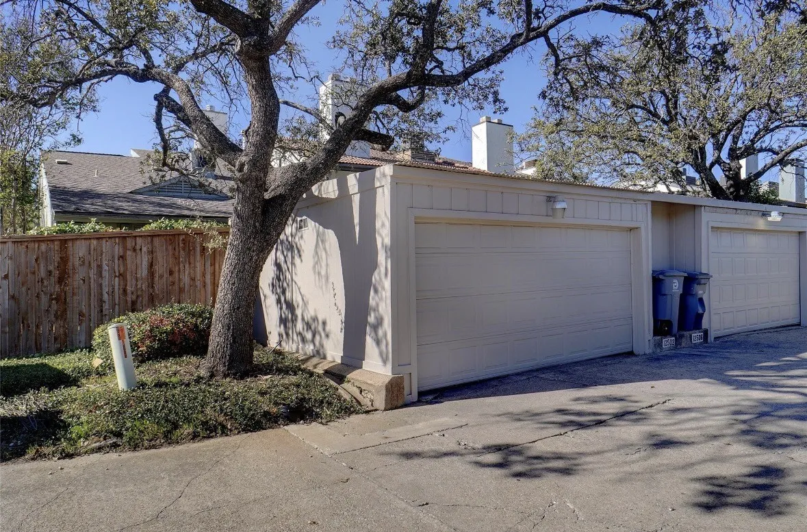 Garage with light-colored door, exterior wall-mounted lighting, and a wood privacy fence