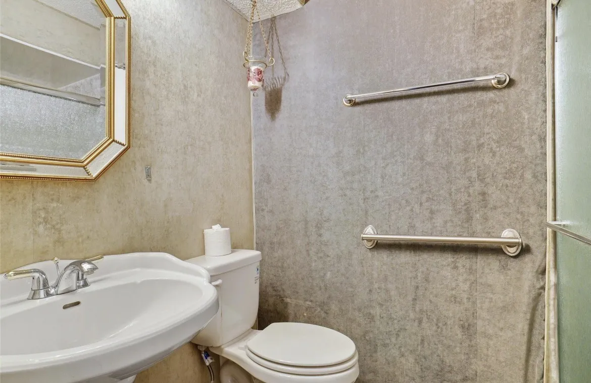 Bathroom 2 Pedestal sink with chrome faucet, wall-mounted mirror, toilet, and two grab bars