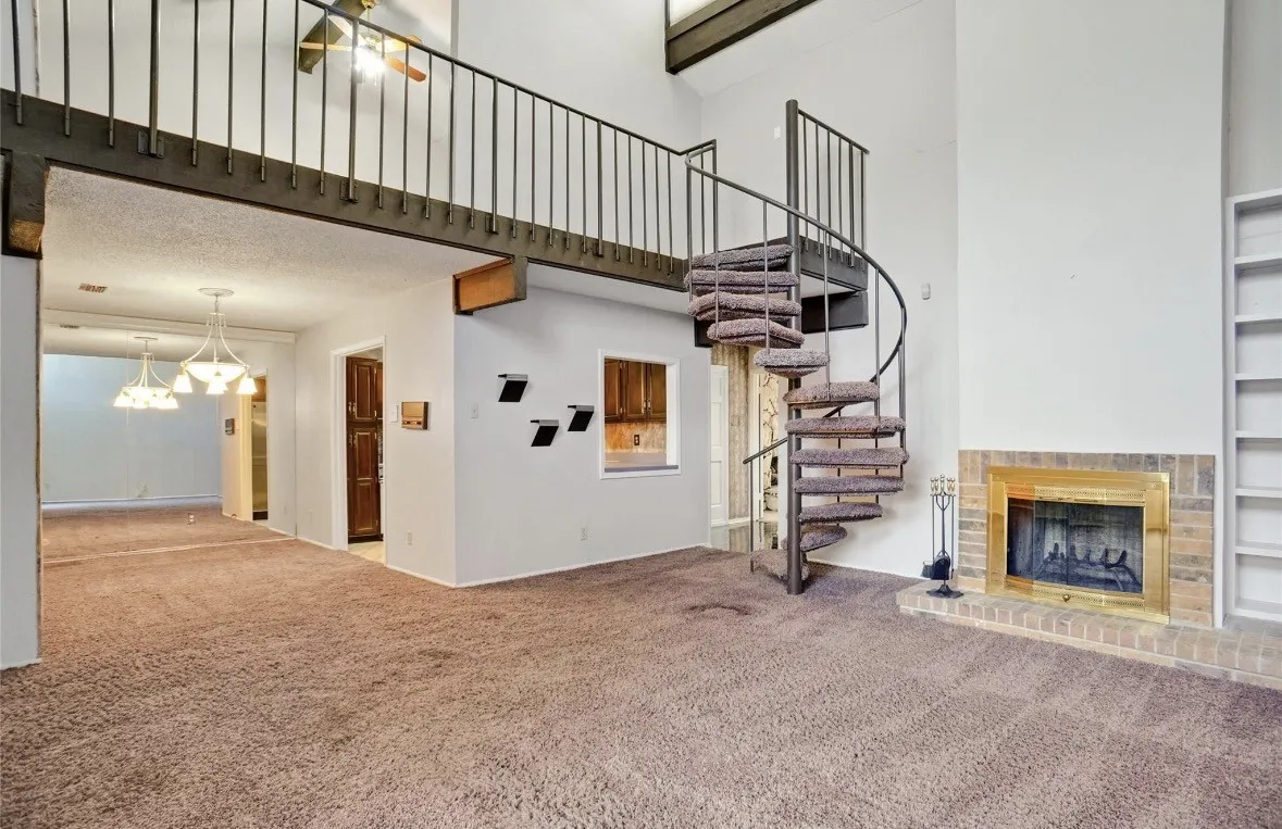 Spiral staircase, brick fireplace with brass surround, built-in shelving, loft area, and vaulted ceilings