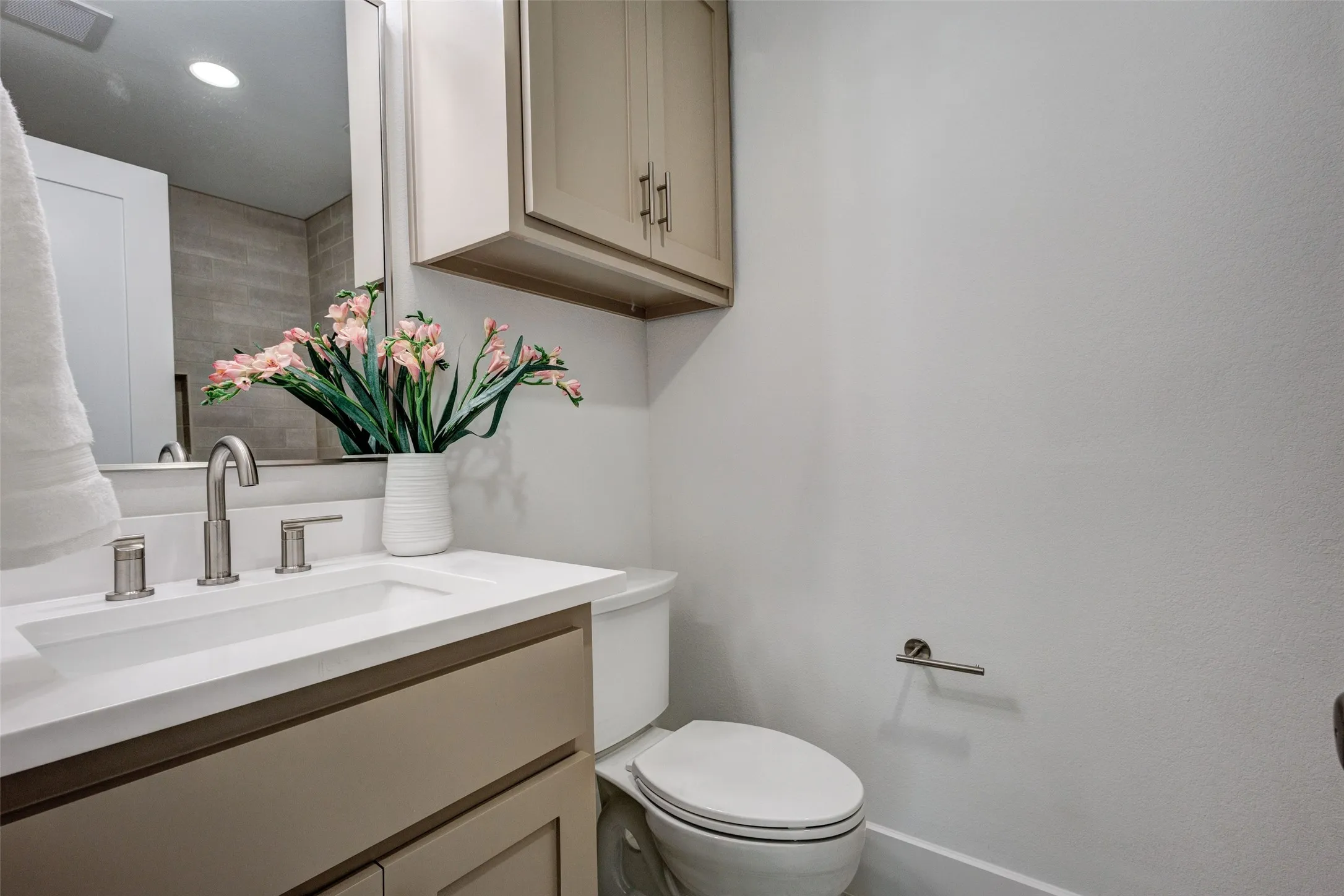 Vanity with integrated sink and brushed nickel faucet, neutral-toned cabinetry, and wall-mounted storage cabinet