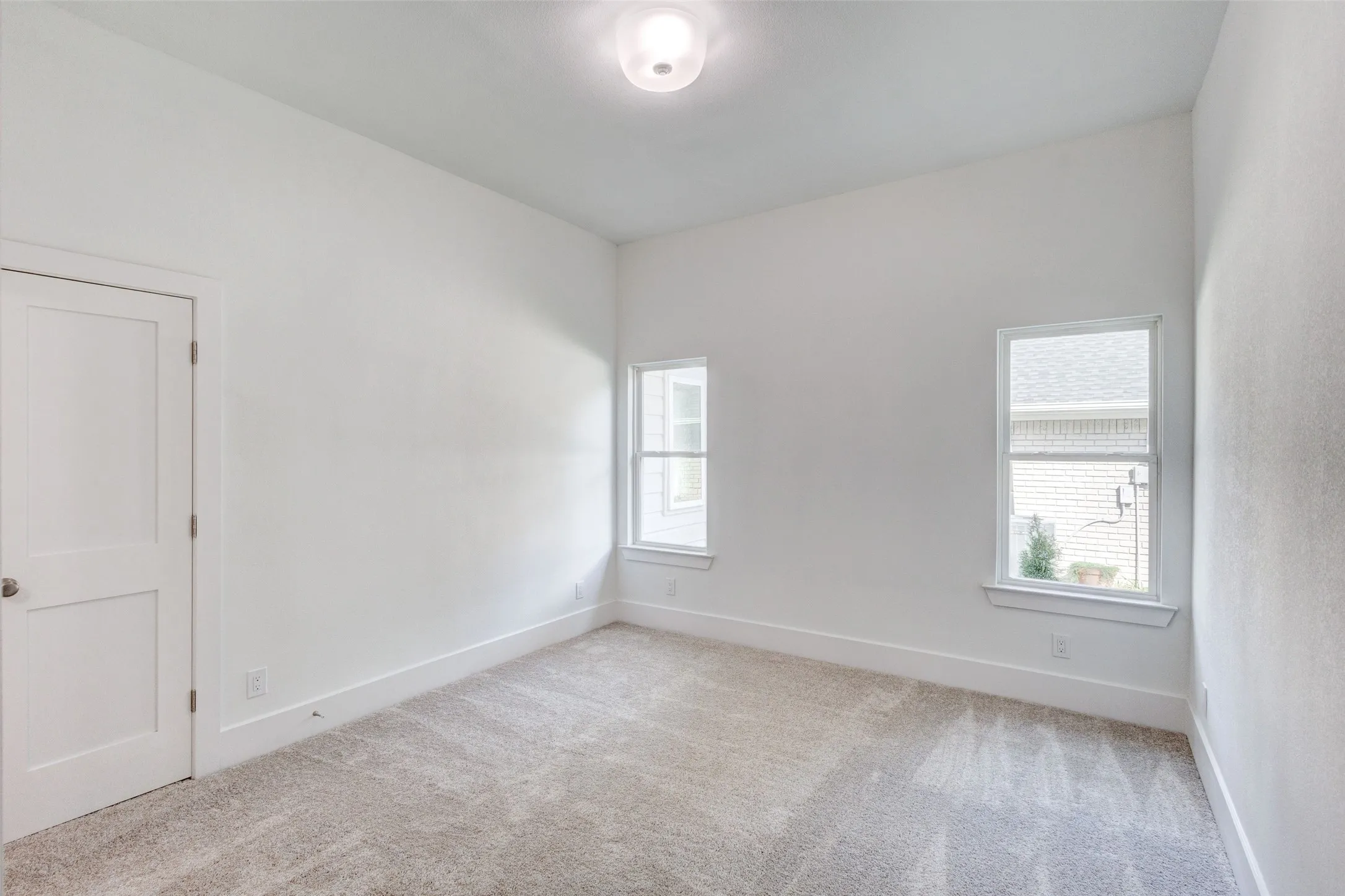 Neutral-toned carpeting with white trim, two white-framed windows, and a flush-mount ceiling light fixture