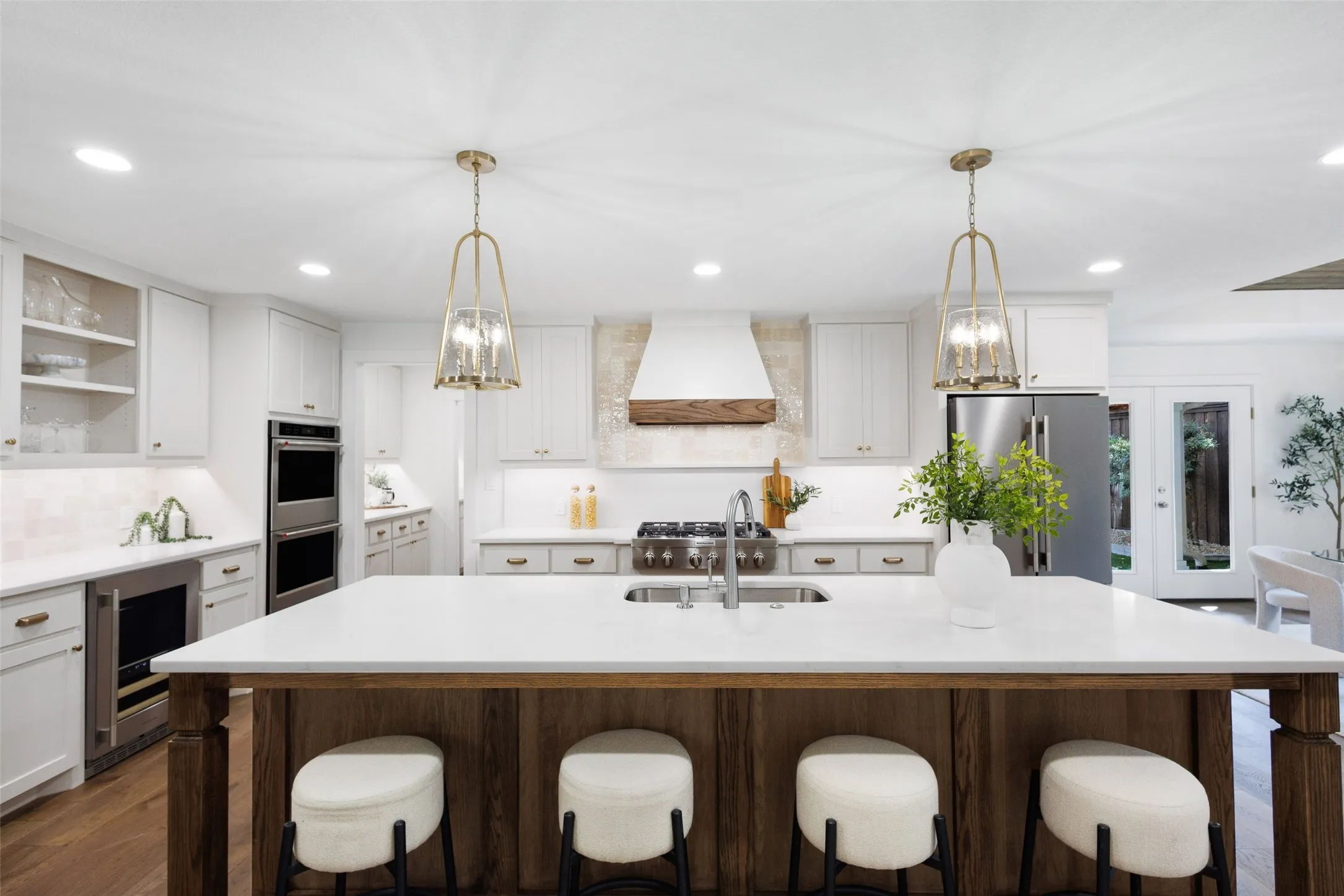 Spacious kitchen featuring a large central island with seating, stainless steel appliances, white cabinetry, and wood-finish flooring