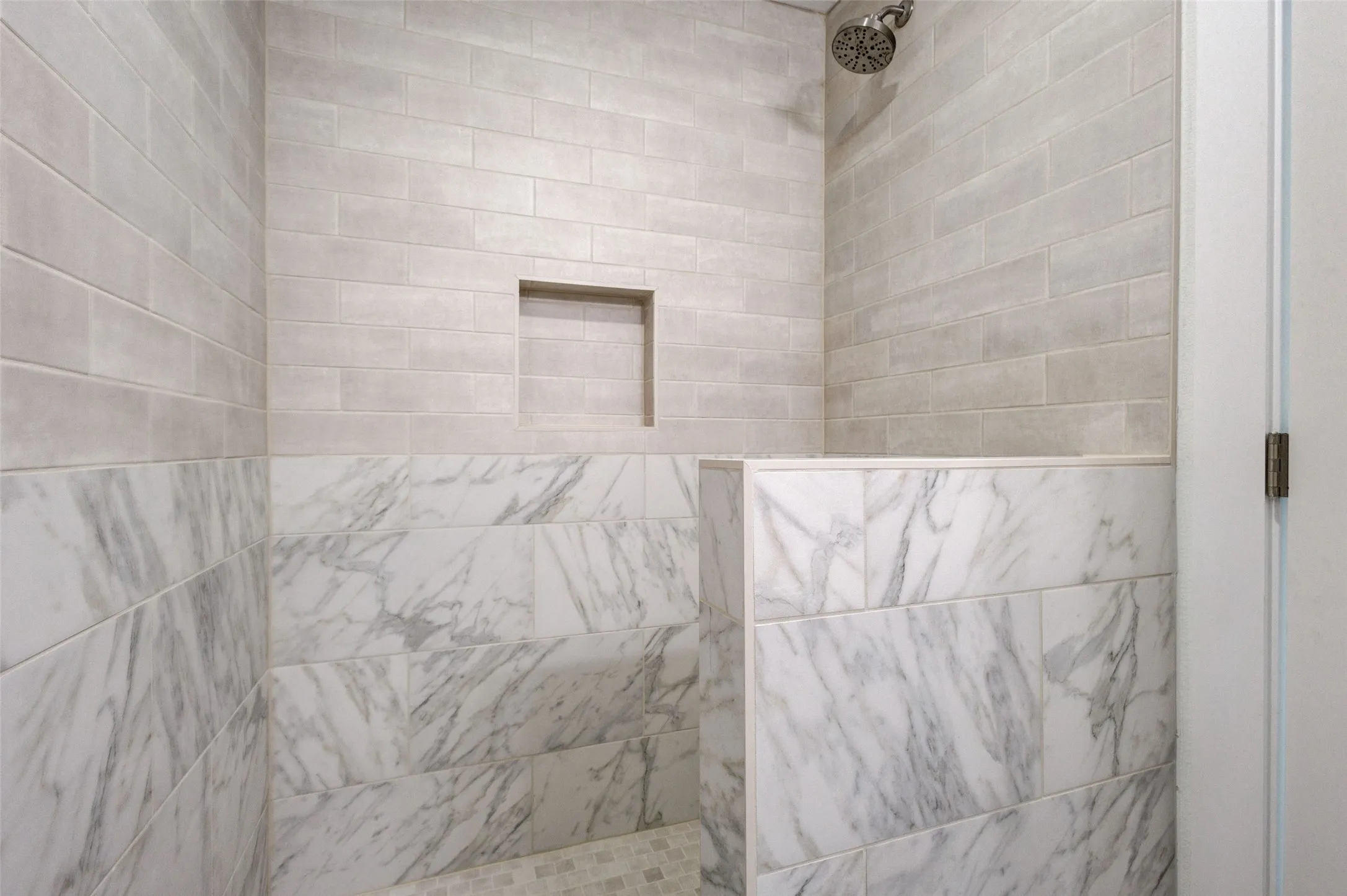 Walk-in shower with a mosaic tile floor, white subway tile walls, a built-in shower niche, and a contrasting marble-look tile accent