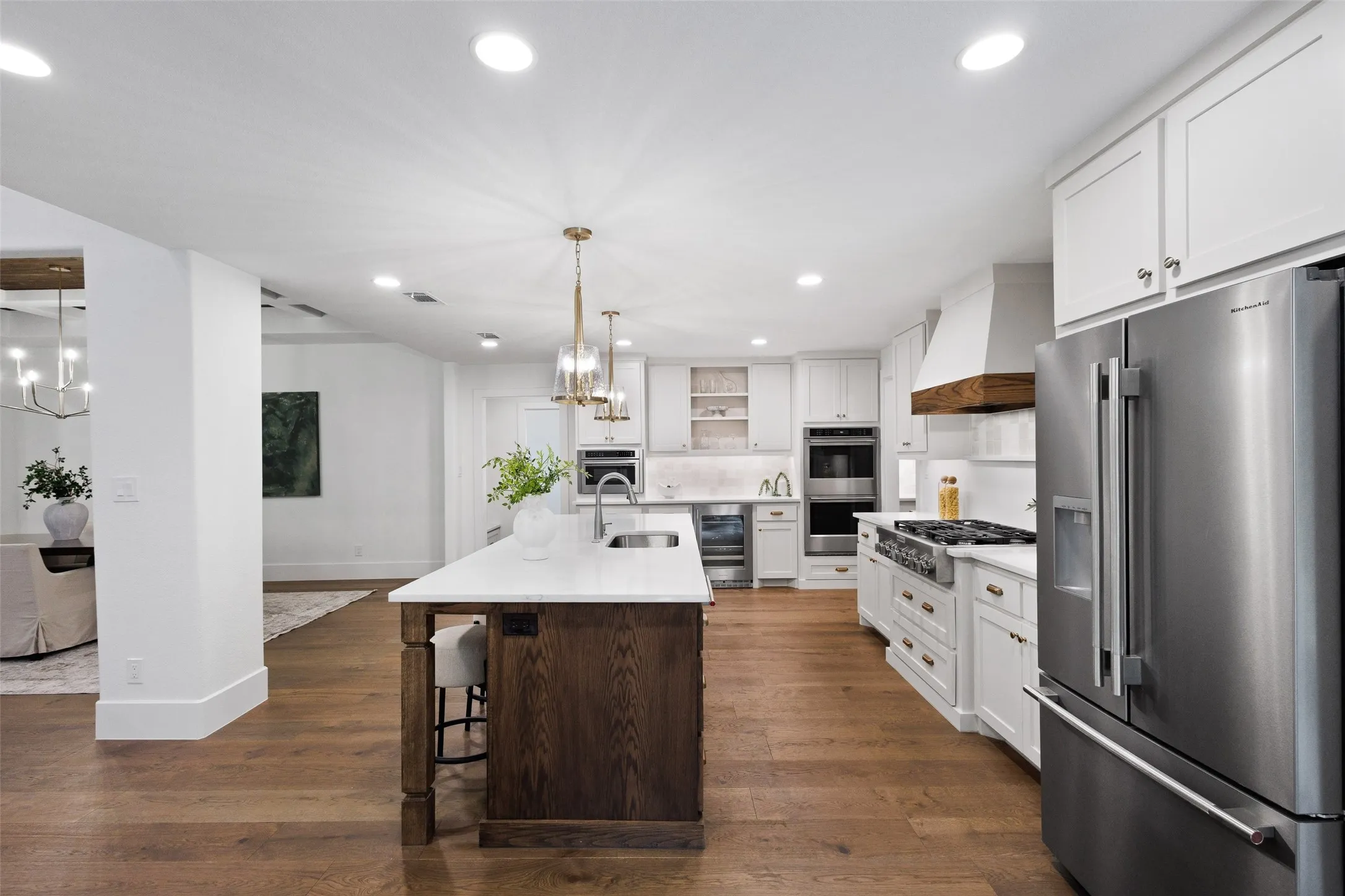 Kitchen featuring a large central island with seating, stainless steel appliances, white cabinetry, and wood-finish flooring
