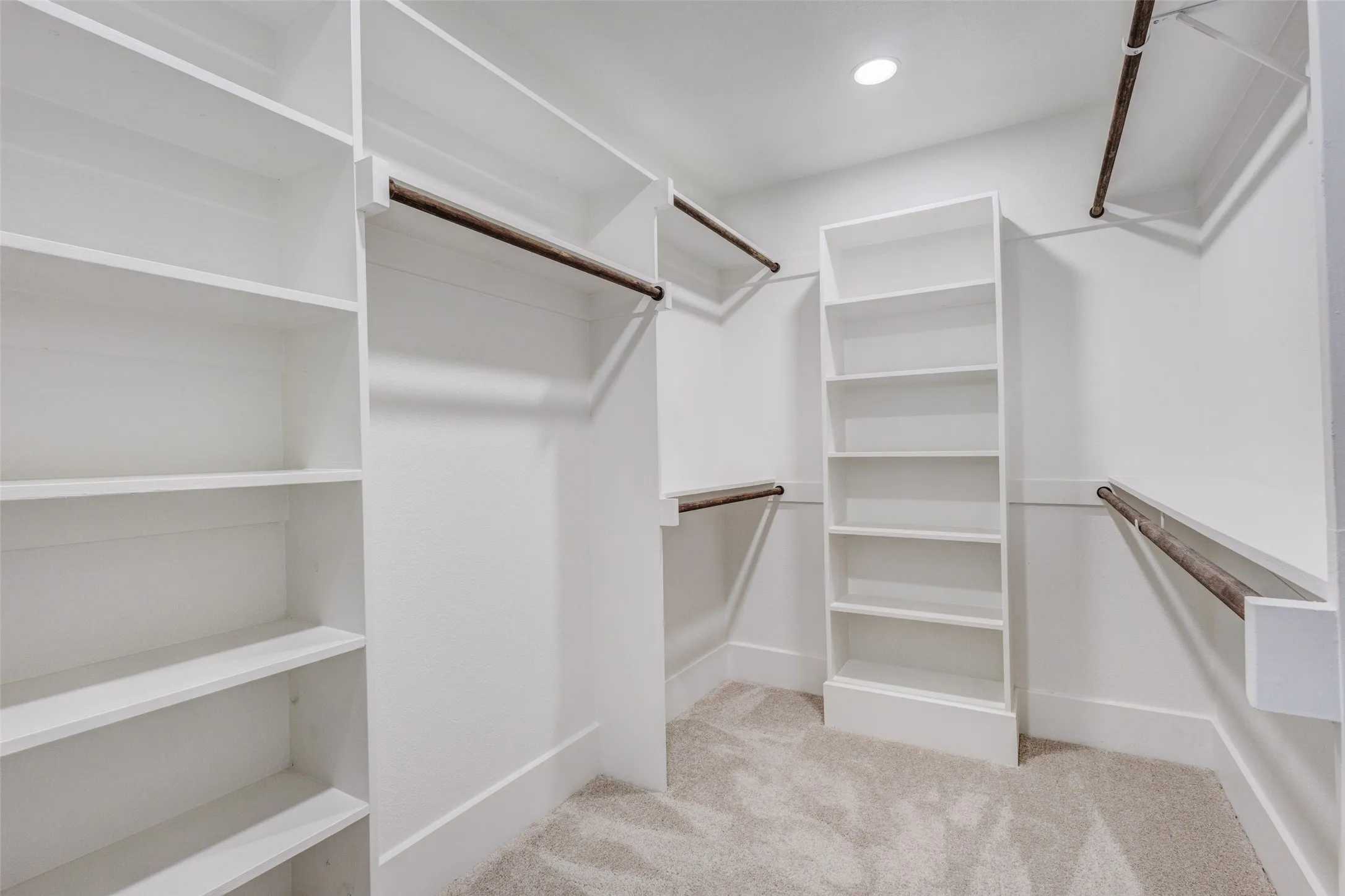 Custom built-in shelving, multiple hanging rods, recessed ceiling lighting, and neutral carpeting