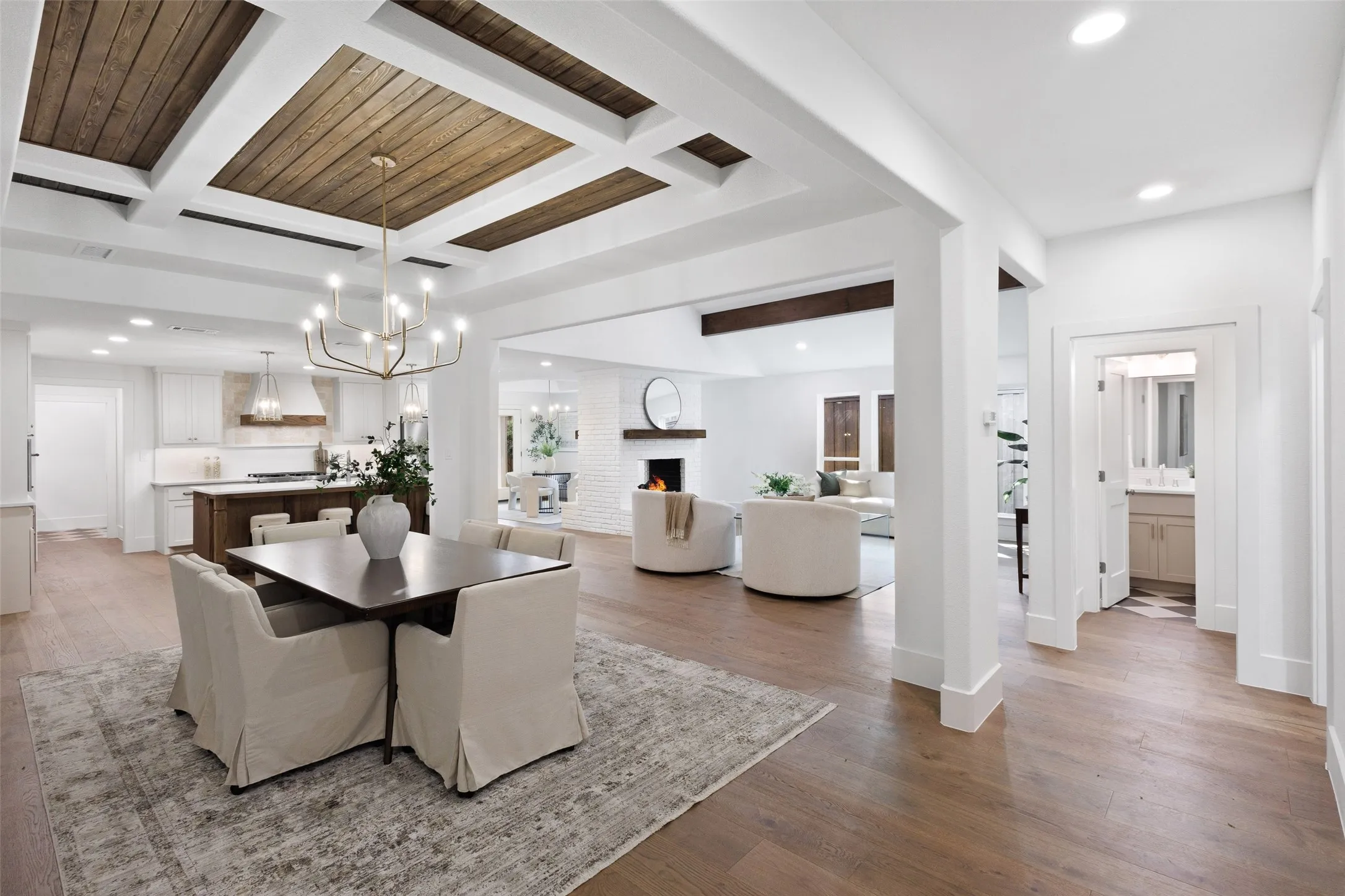 Wood-finish flooring throughout, coffered ceiling with wood paneling, recessed lighting, white brick fireplace, and built-in cabinetry