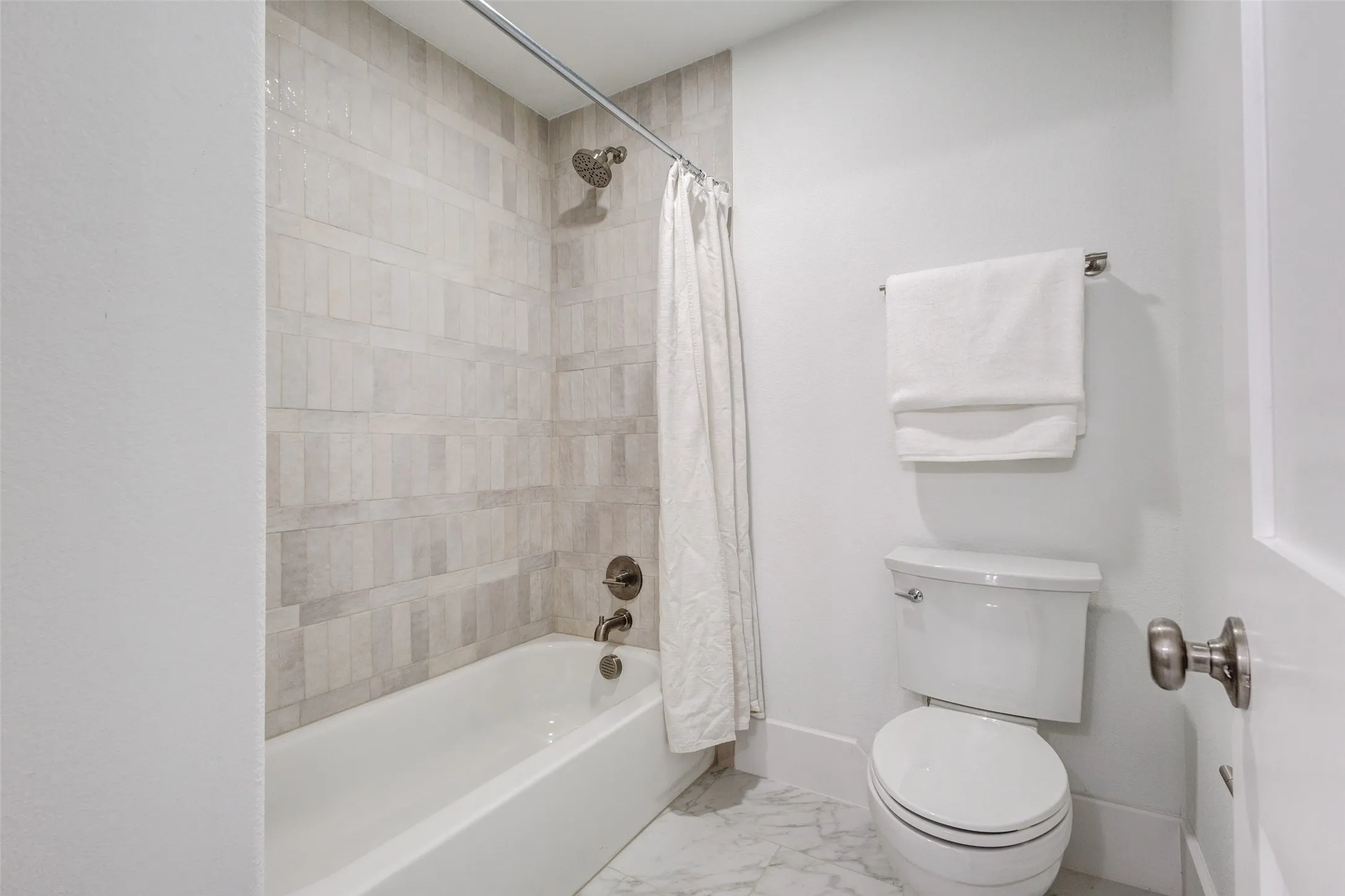 Bathtub with tiled surround, brushed nickel fixtures, and a white toilet