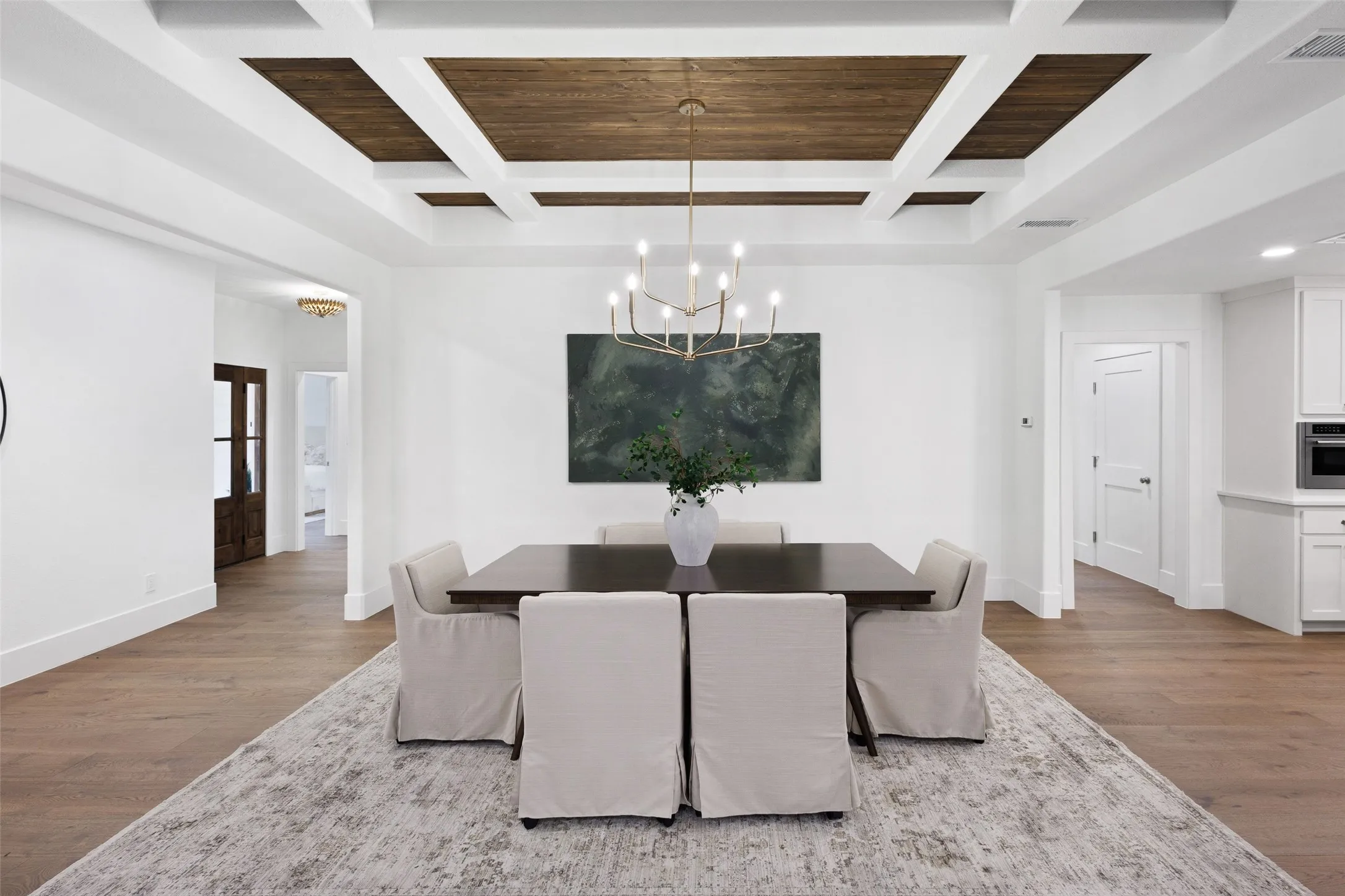Coffer ceiling with wood-finish inserts, light wood-finish flooring, and a gold-tone chandelier