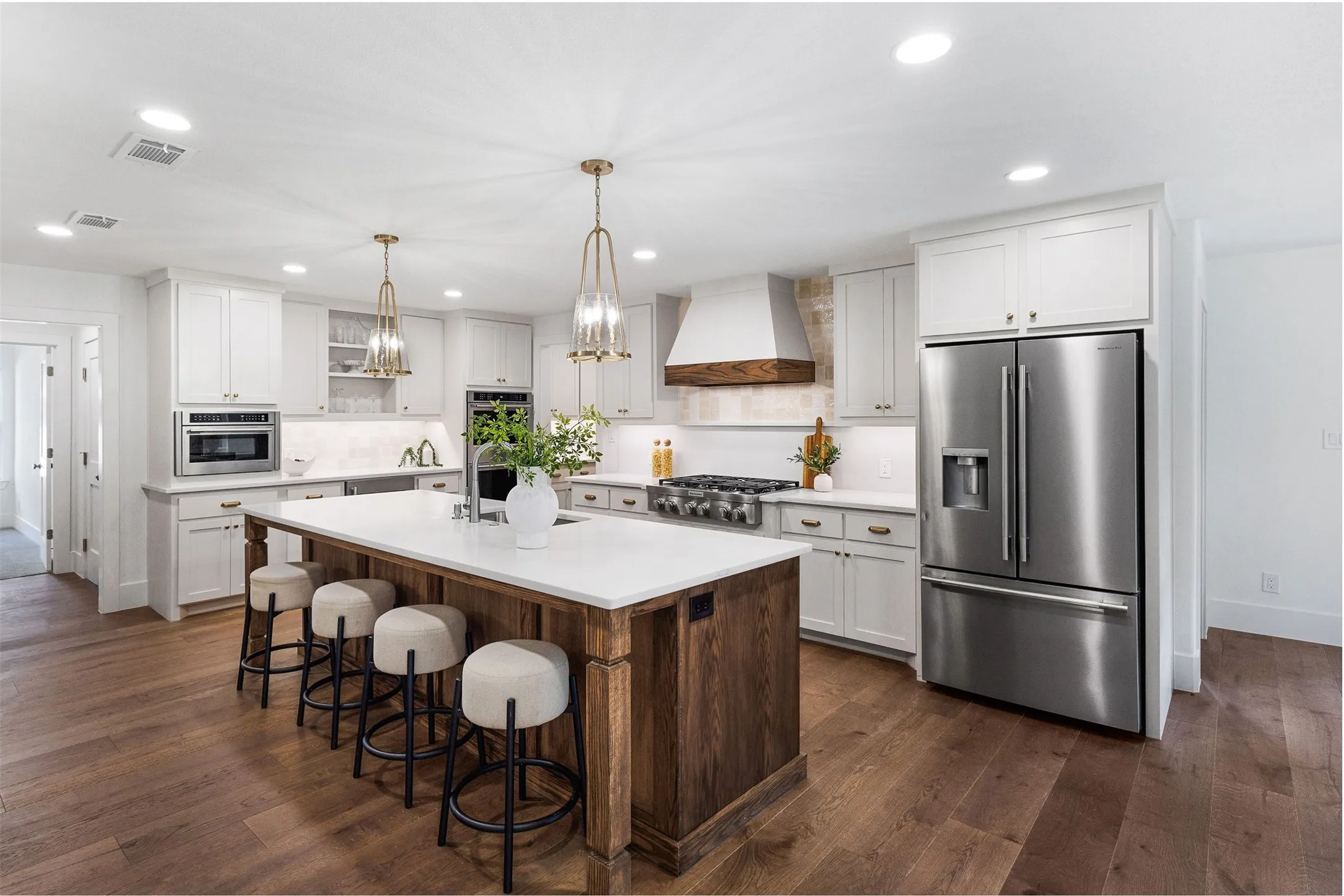 Spacious kitchen featuring an expansive center island with seating, white shaker cabinetry, stainless steel appliances, and wood-finish flooring