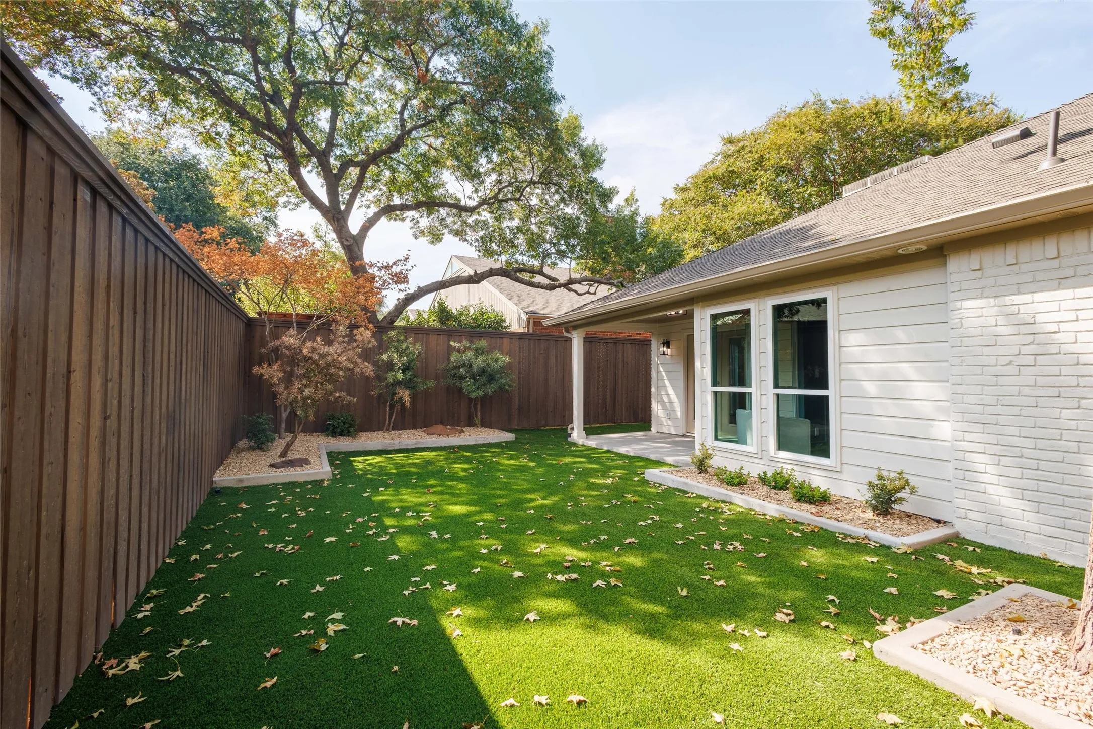 Private backyard featuring a tall privacy fence, covered patio, artificial turf, and mature landscaping