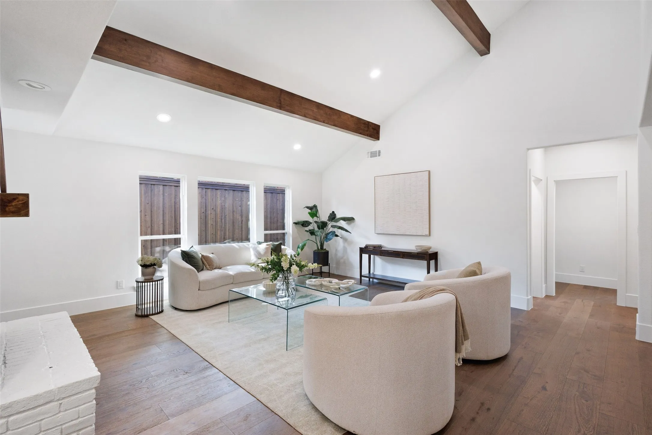 Vaulted ceiling with exposed wood beams, wood-finish flooring, recessed lighting, and a white painted brick fireplace surround