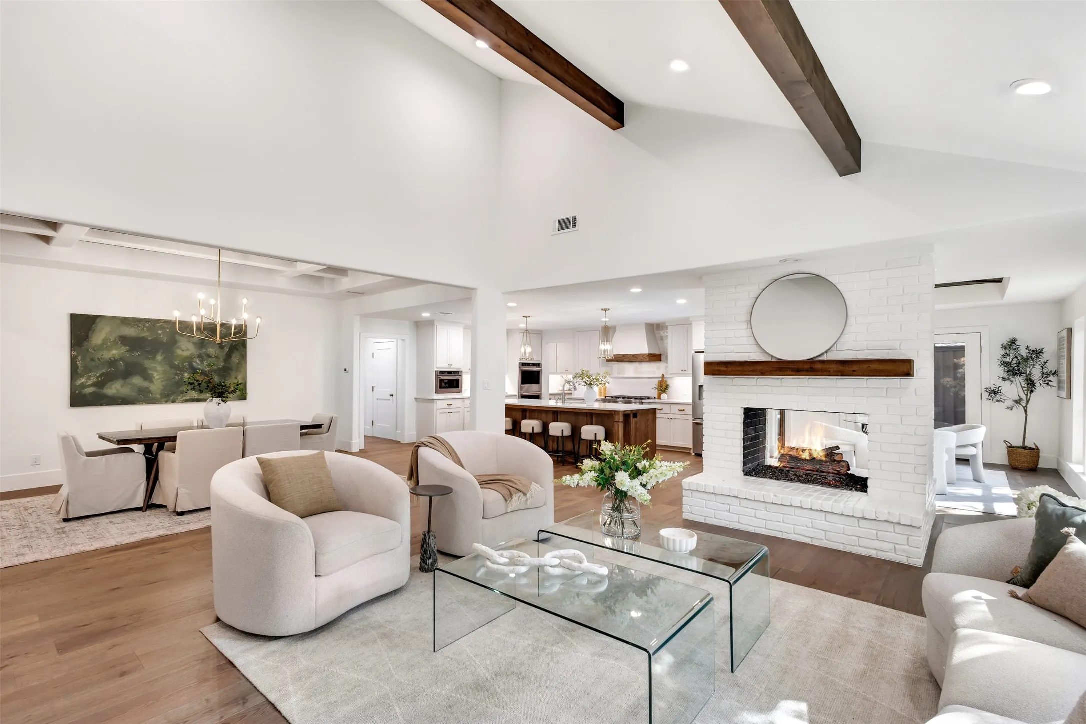 Vaulted ceiling with exposed wood beams, wood-finish flooring, white brick fireplace with wood mantle, recessed lighting, and kitchen with island