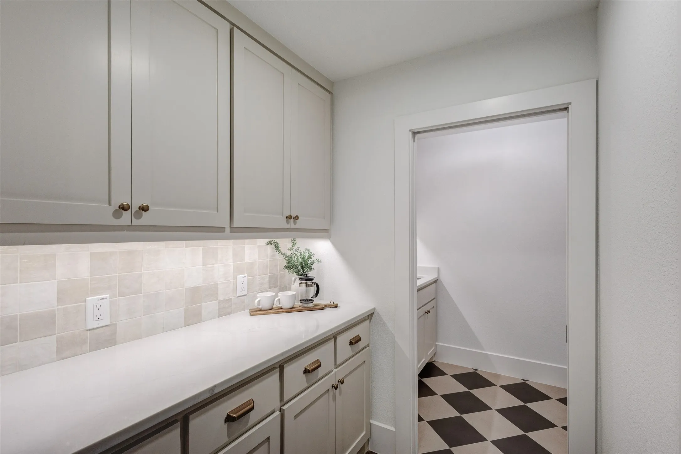 Built-in cabinetry with under-cabinet lighting, light-toned countertop, square tiled backsplash, and checkerboard floor