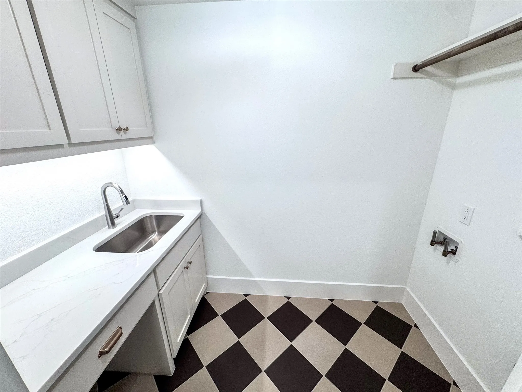 White shaker-style cabinetry with undermount lighting, stainless steel sink with gooseneck faucet, light-toned countertop, and checkerboard floor tiling