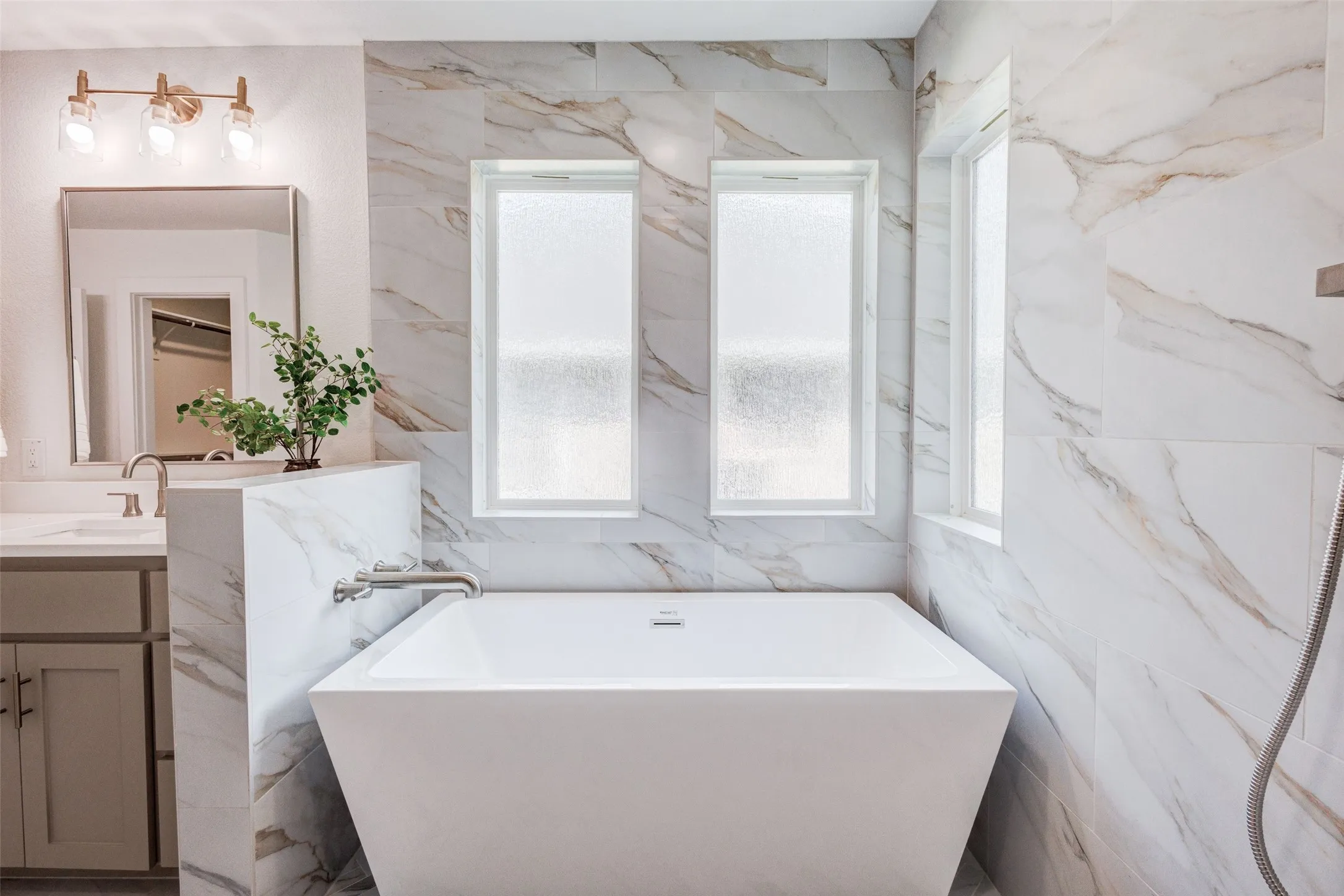 Freestanding soaking tub with a wall-mounted faucet, surrounded by large format tile with natural veining