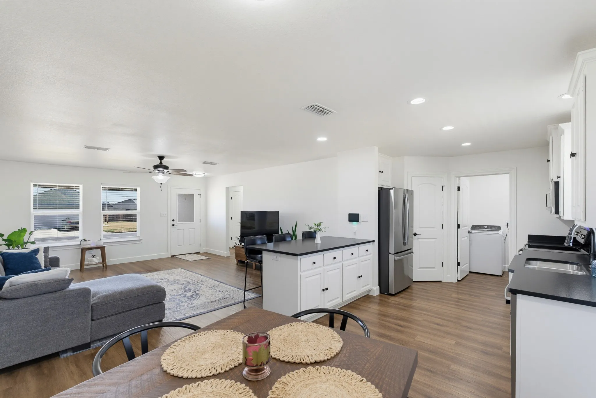 Open-concept living area featuring wood-finish flooring, recessed lighting, white cabinetry with dark hardware, and a center island with countertop seating