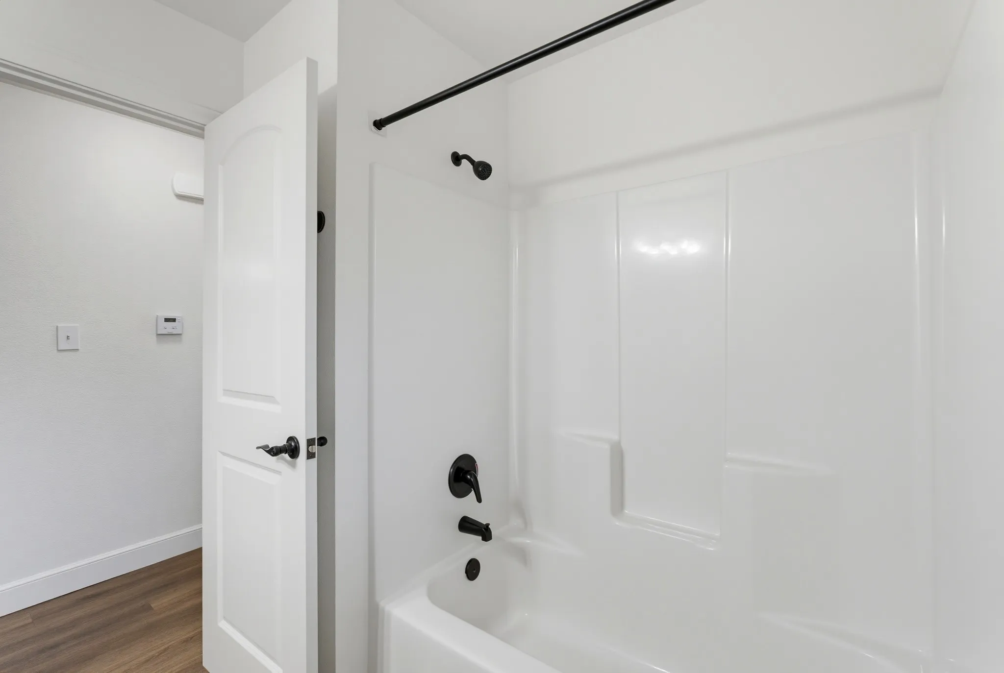 White tub and shower combination with black fixtures and a white paneled door