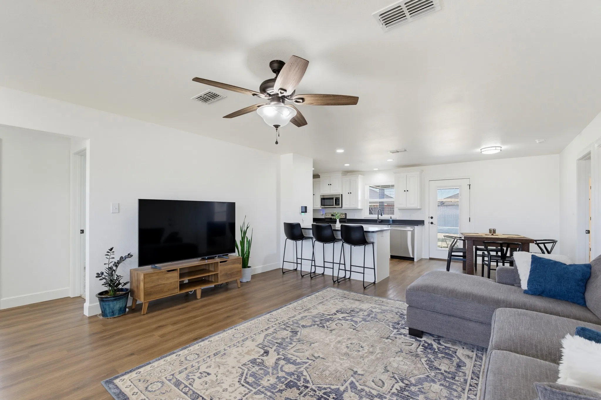 Open-concept living area featuring wood-finish flooring, a ceiling fan with integrated lighting, white walls, and recessed lighting