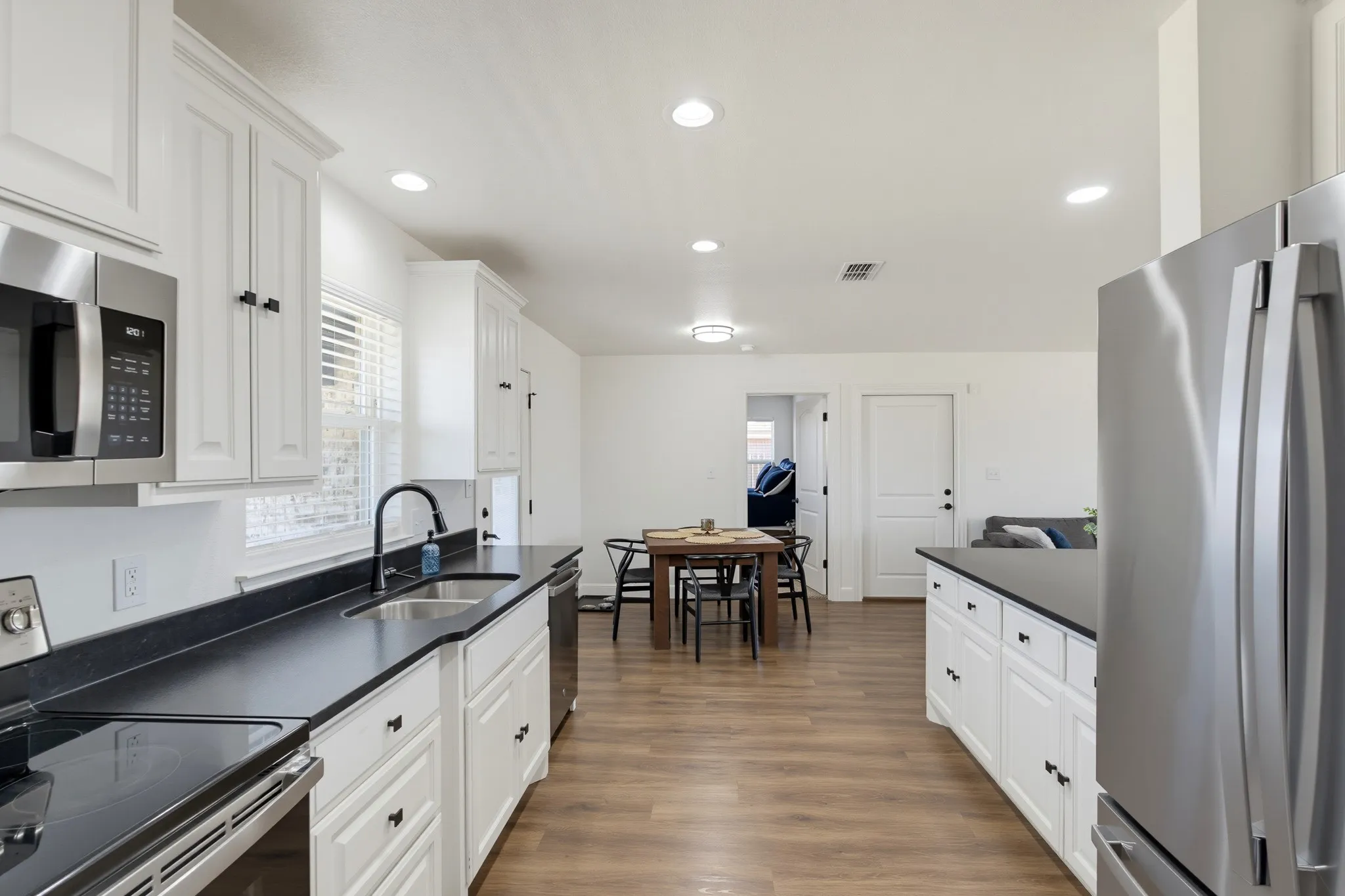 Kitchen featuring white cabinetry, dark countertops, a stainless steel microwave, a stainless steel sink, and wood-finish flooring