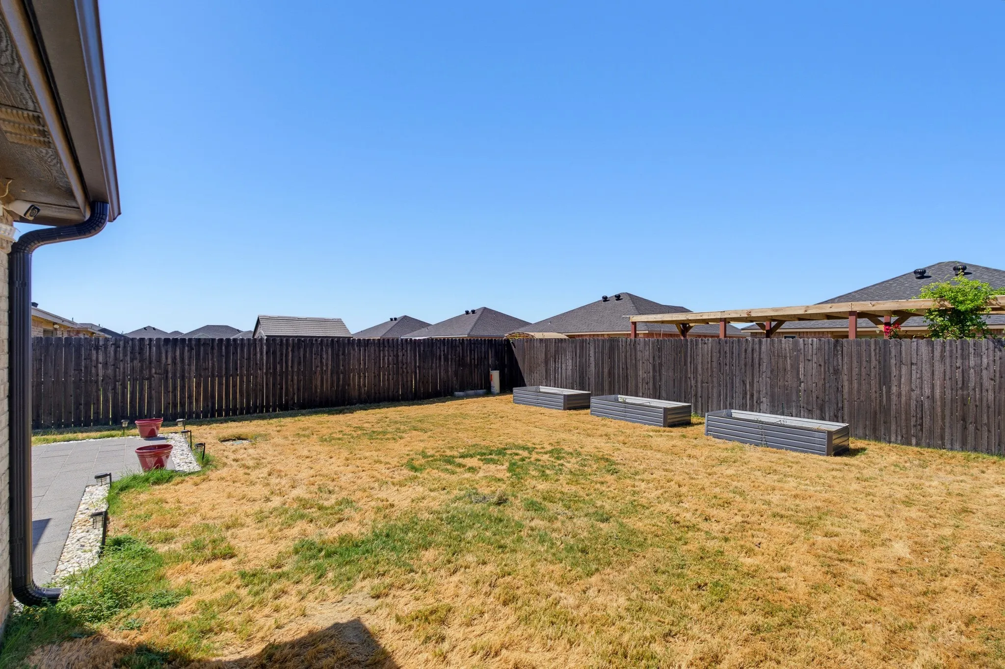 Fenced backyard featuring three raised garden beds, a paved patio area, and a dark stained privacy fence