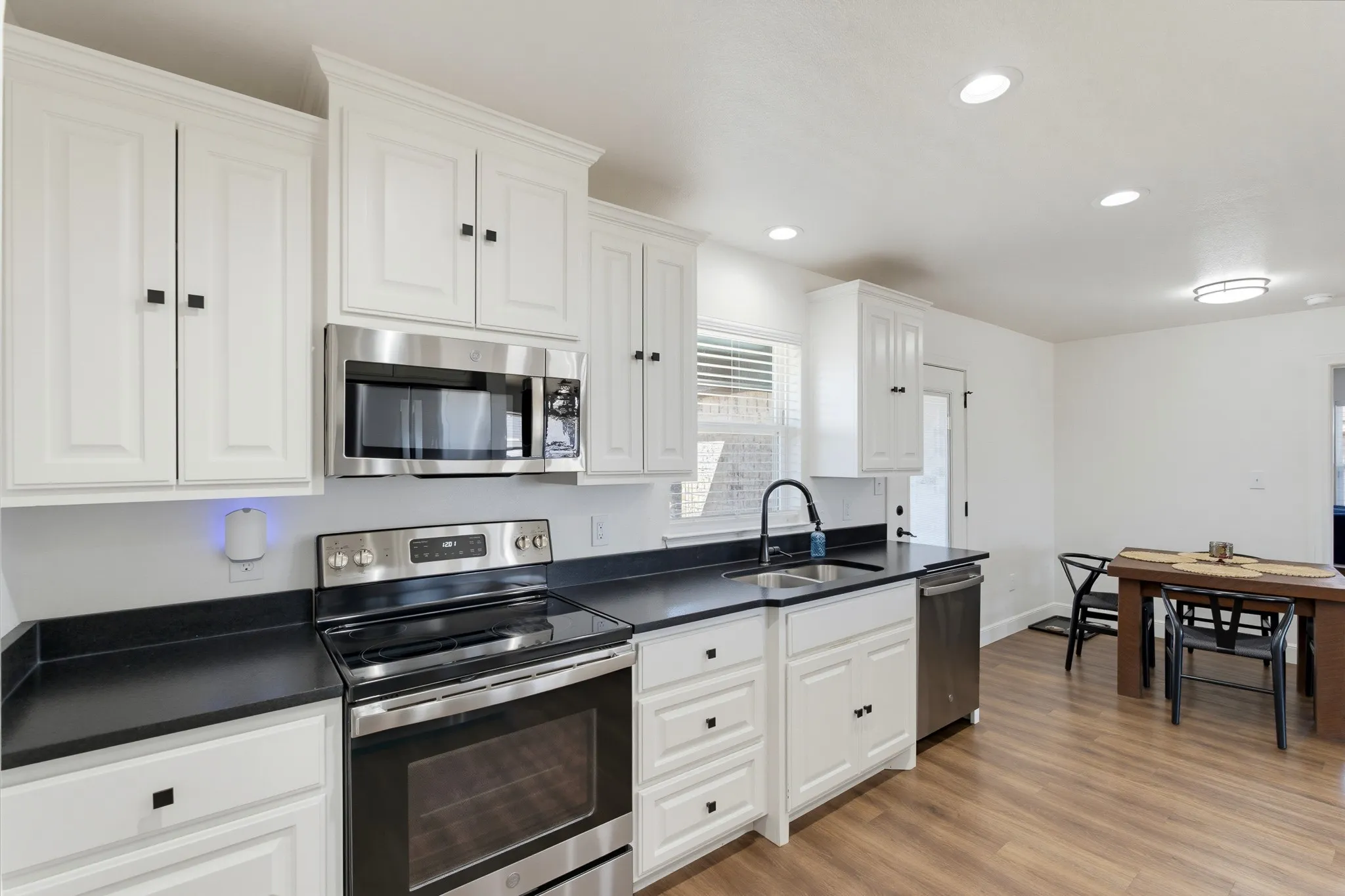 White shaker-style cabinetry with dark hardware, stainless steel appliances, dark countertops, and wood-finish flooring
