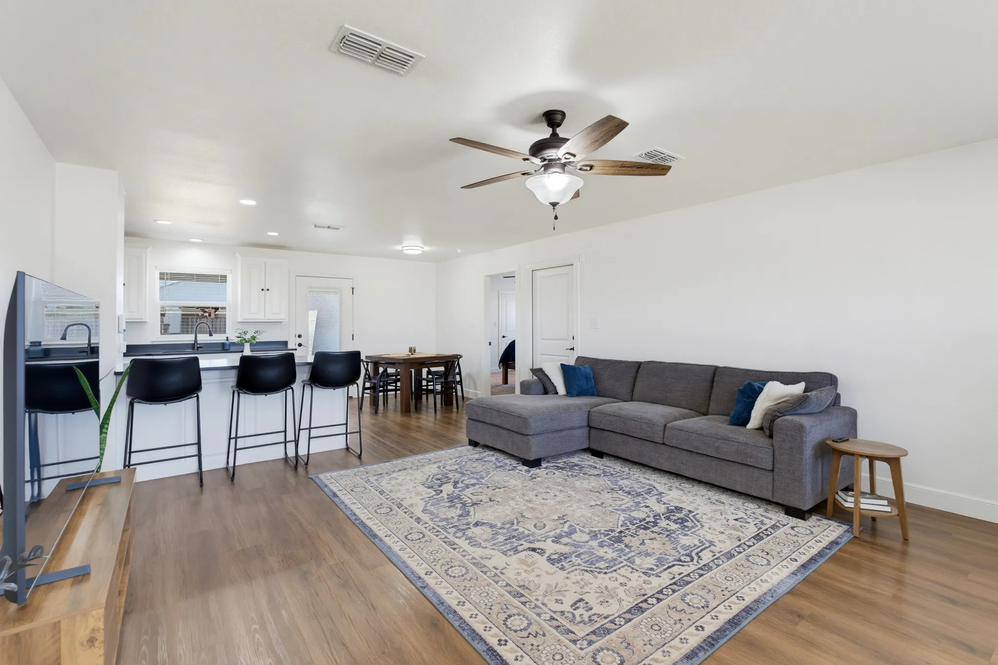Wood-finish flooring, white walls, ceiling fan with light fixture, kitchen island with dark countertop, built-in white cabinetry