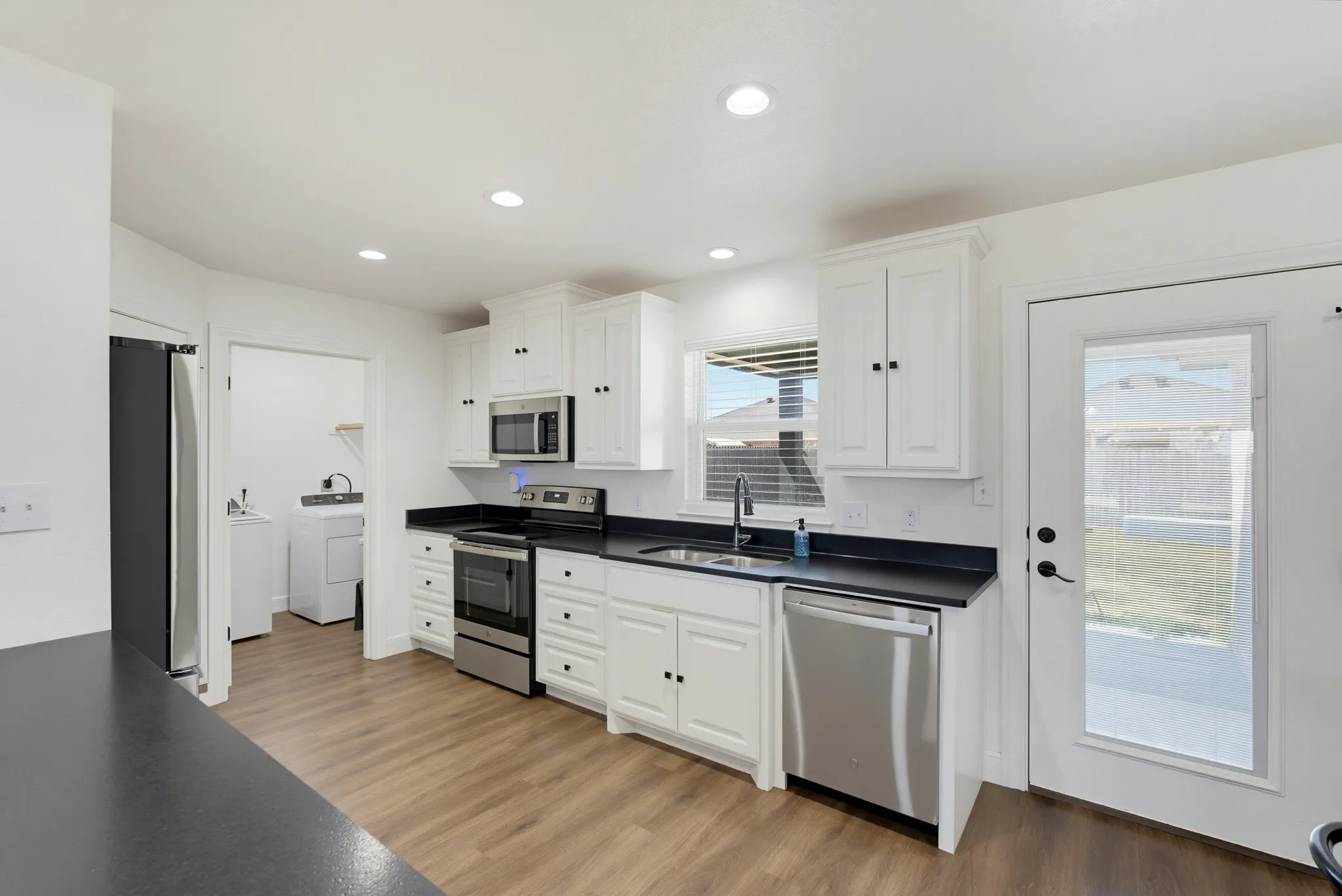 Kitchen featuring white cabinetry, dark countertops, stainless steel appliances, wood-finish flooring, and recessed lighting