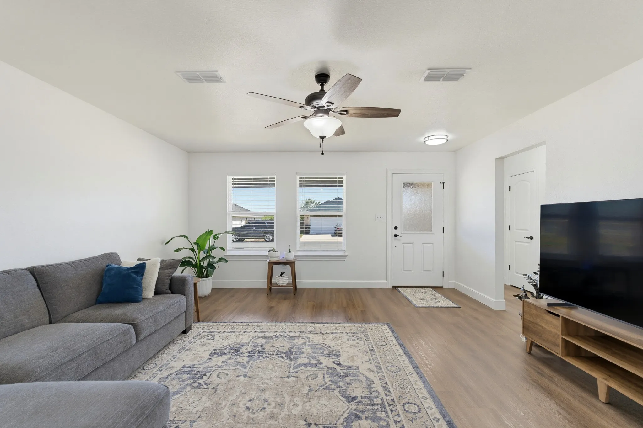 Bright interior with wood-finish flooring, white walls, and a ceiling fan with integrated lighting