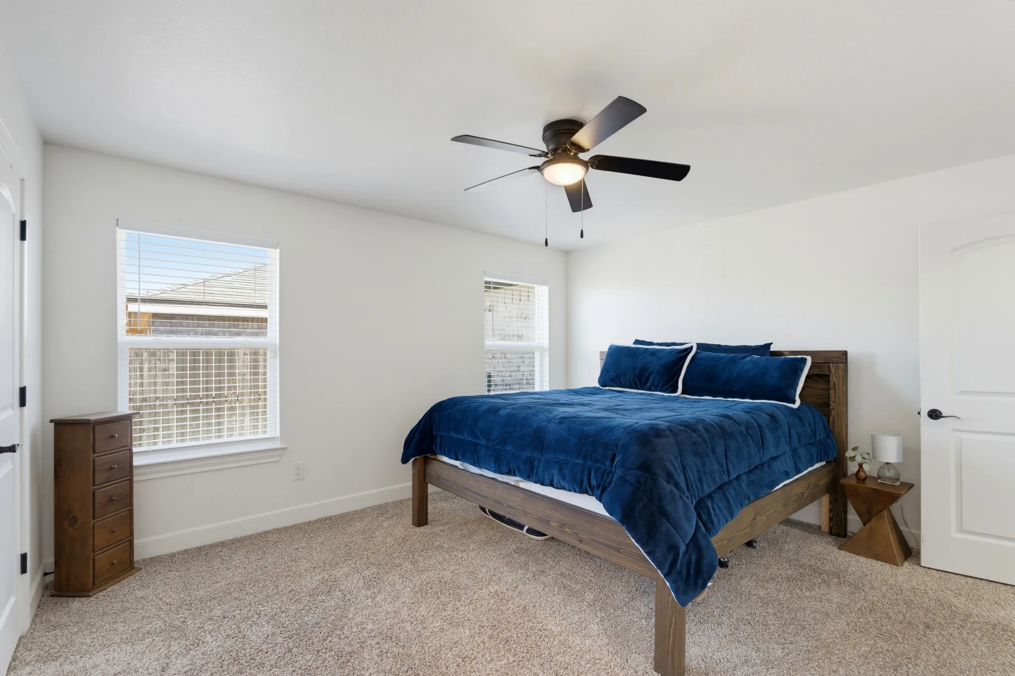 Recessed windows, neutral wall tones, textured carpeting, modern ceiling fan with integrated lighting, and a paneled interior door with dark hardware