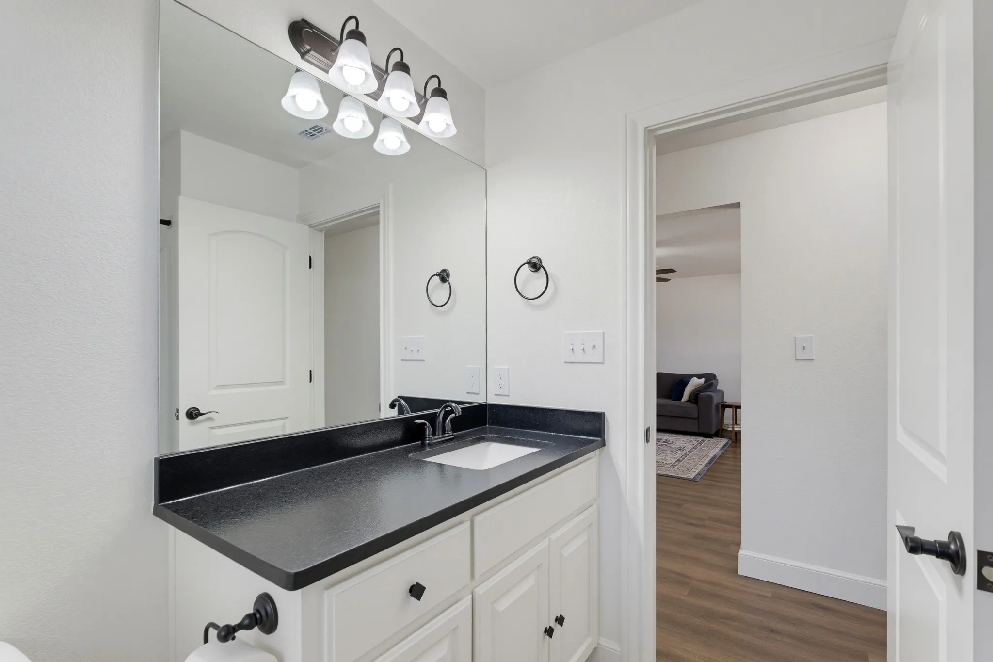 White vanity with shaker-style cabinetry, dark countertop, and integrated sink