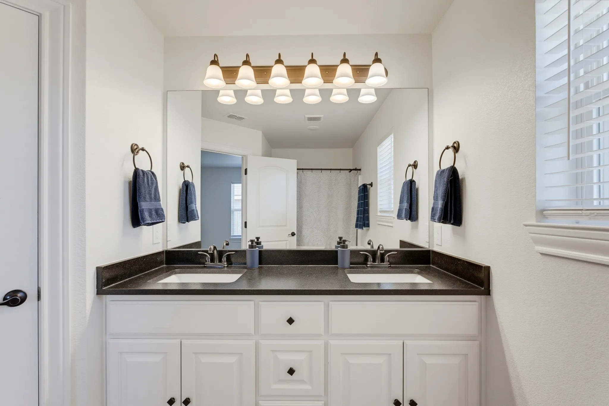 Double vanity with white cabinetry, dark countertop, dual undermount sinks, and a framed mirror