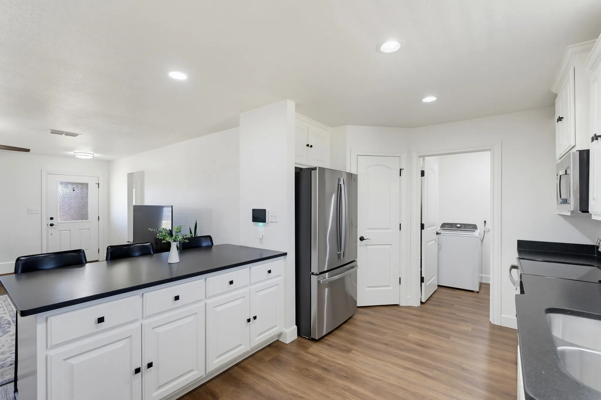 Modern kitchen featuring white cabinetry, dark countertops, wood-finish flooring, and recessed lighting