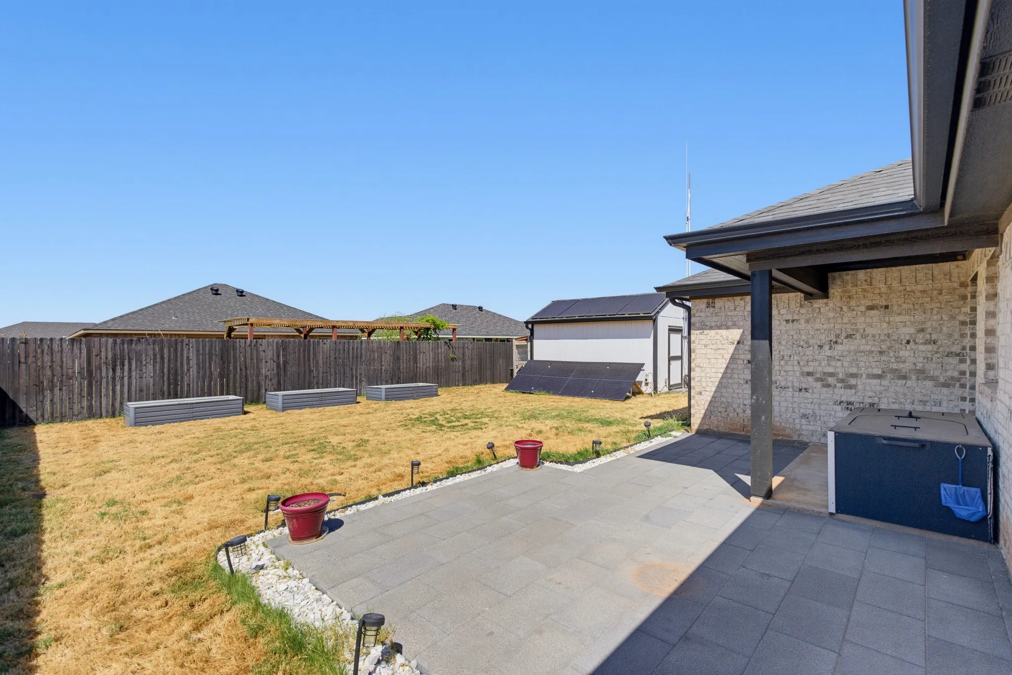 Expansive backyard with a full privacy fence, paved patio, covered outdoor living area, and an accessory building