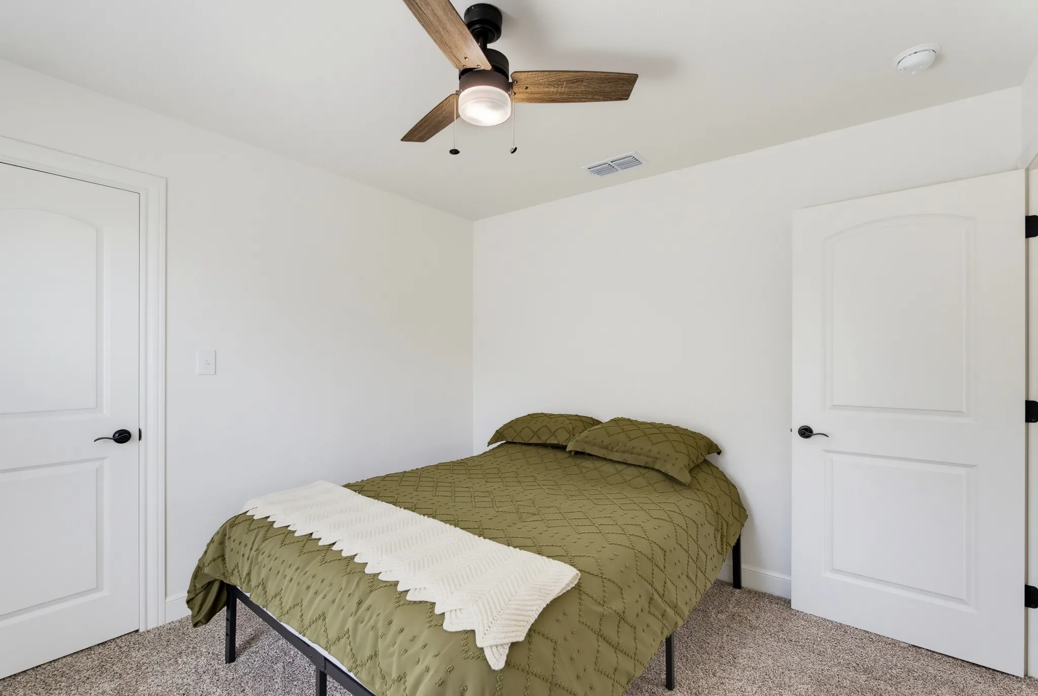 Carpeted room featuring a ceiling fan with light, and two white doors with arched panels and black​​‌​​​​‌​​‌‌​‌‌​​​‌‌​‌​‌​‌​​​‌​​ hardware