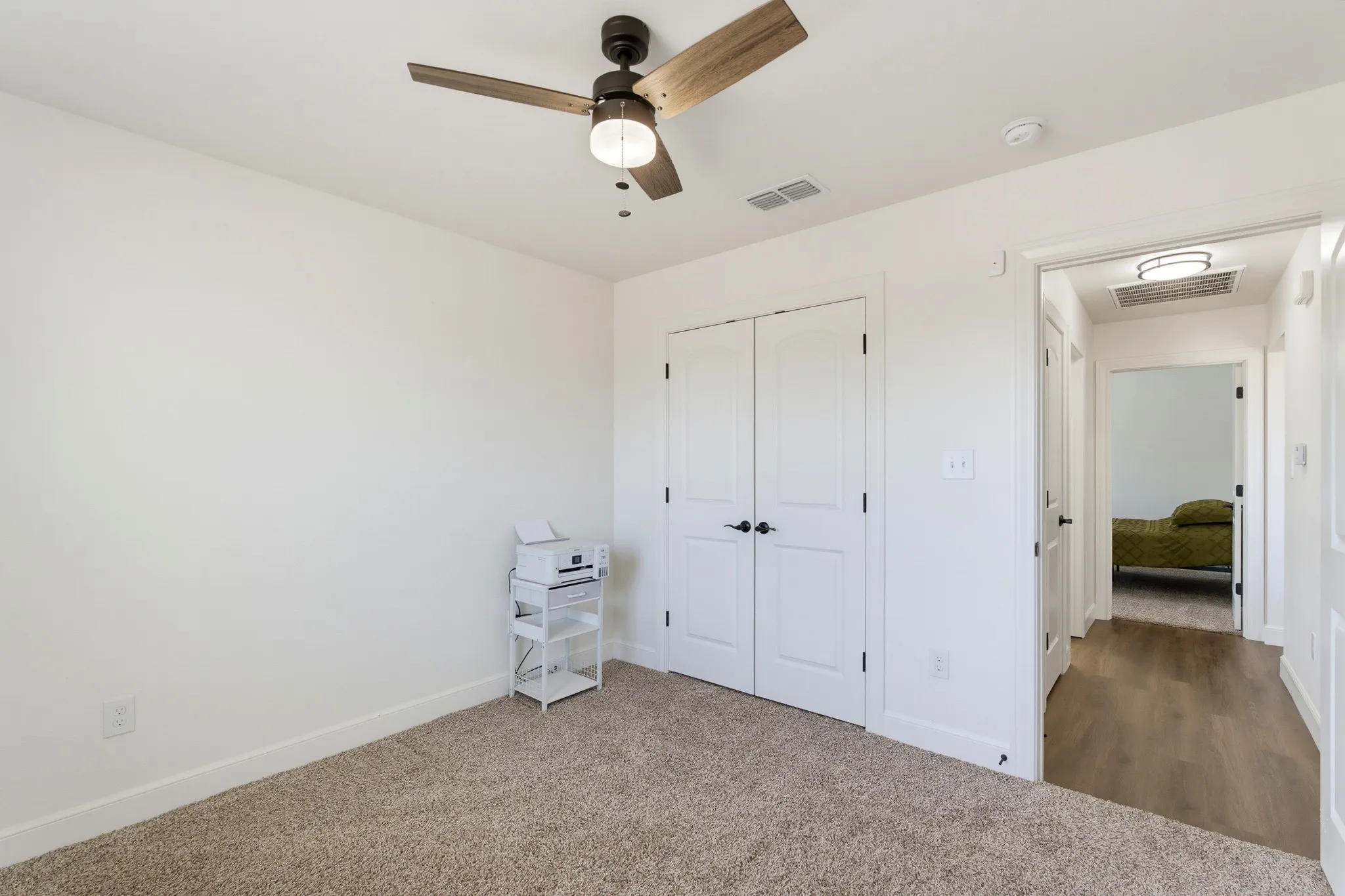 Carpeted room with a ceiling fan, dual panel closet doors, and light neutral wall finishes