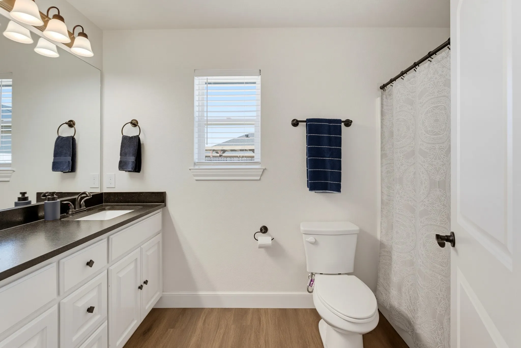 White vanity with dark countertop and integrated sink, bronze-finish faucet, and wood-finish flooring