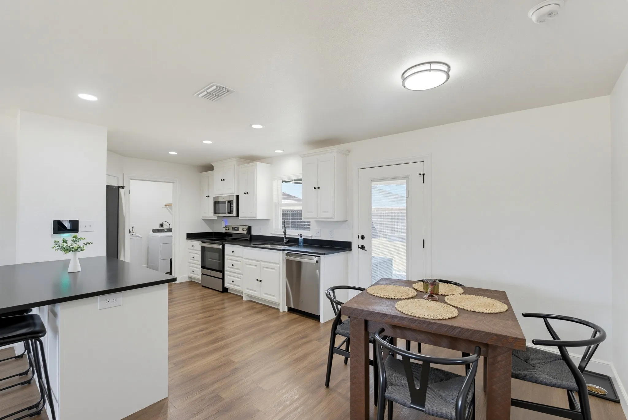 Open-concept kitchen featuring white cabinetry, stainless steel appliances, black countertops, and wood-finish flooring