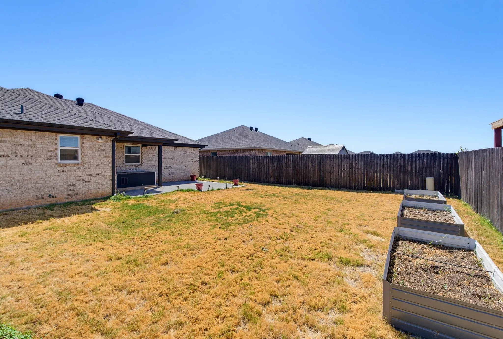 Rear exterior featuring a brick facade, covered patio, dark wood privacy fencing, and multiple raised garden beds