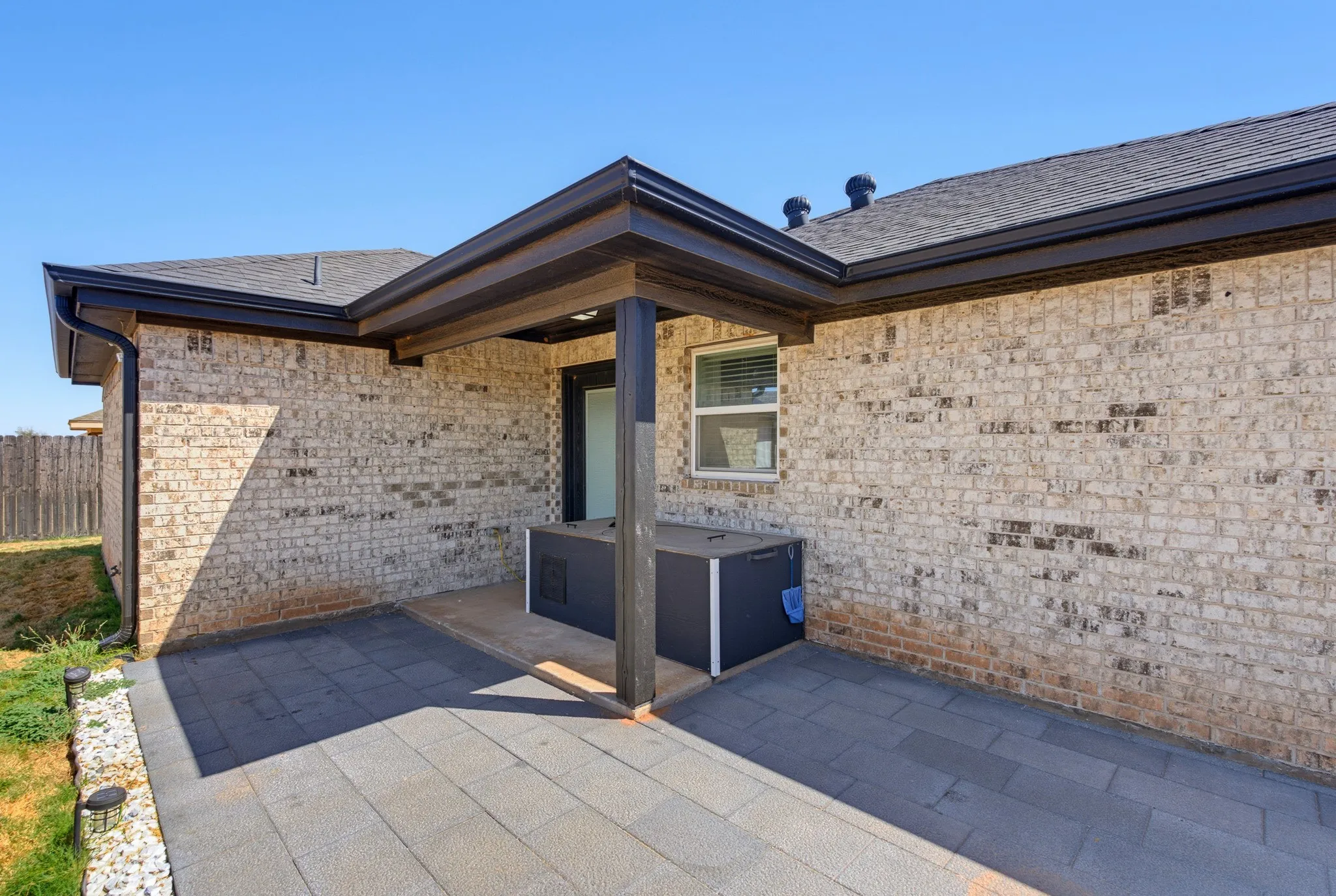 Covered patio featuring a dark grey paver surface, light-colored brick exterior, and dark gutters