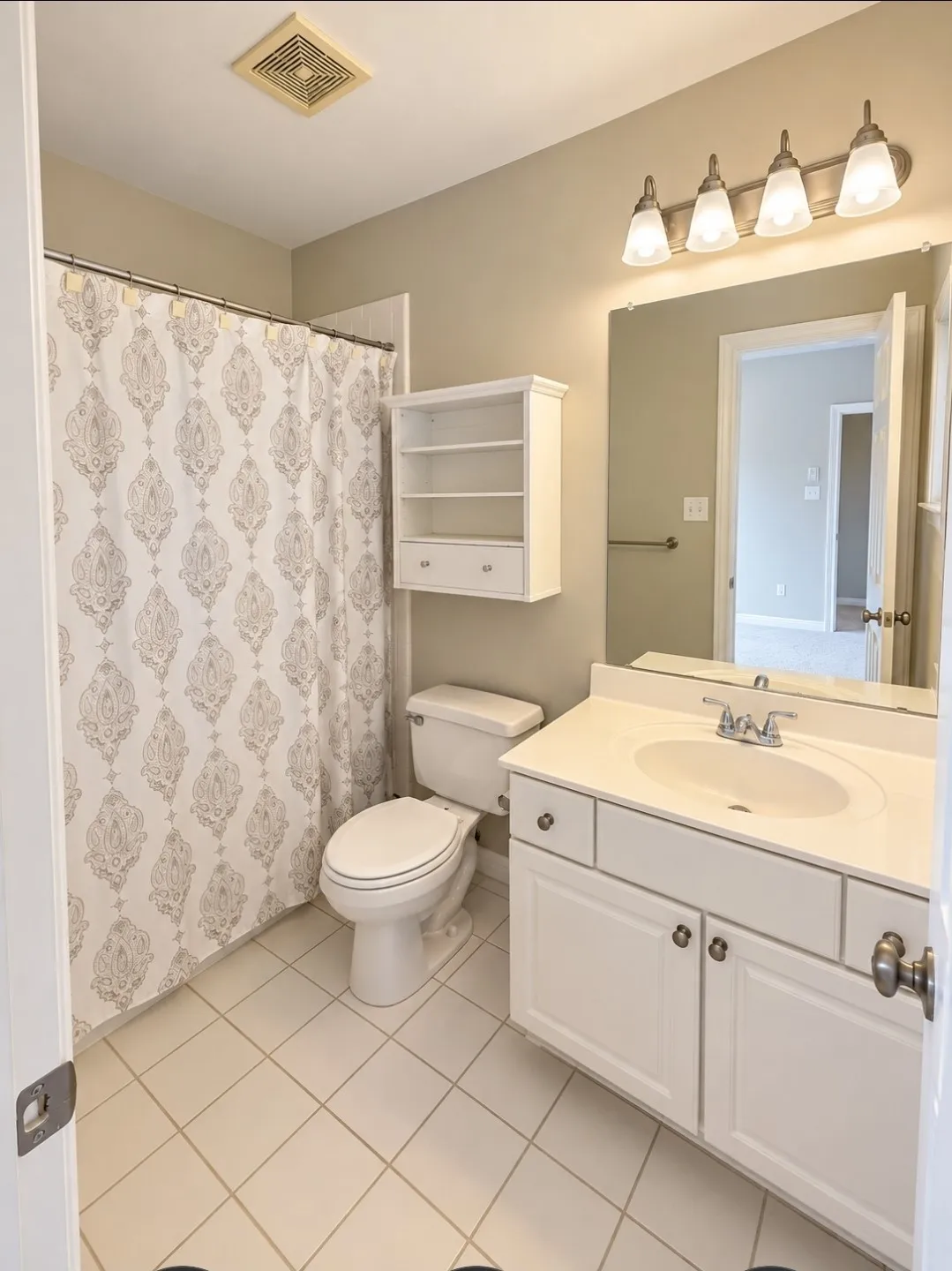 White tile flooring, white vanity with integrated sink, four-light vanity fixture, built-in wall cabinet, and wall-mounted mirror