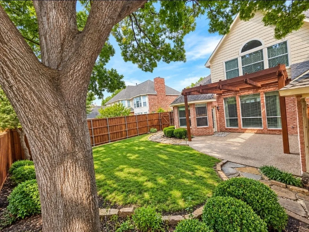 Expansive backyard featuring a manicured lawn, established tree, and a wooden privacy fence
