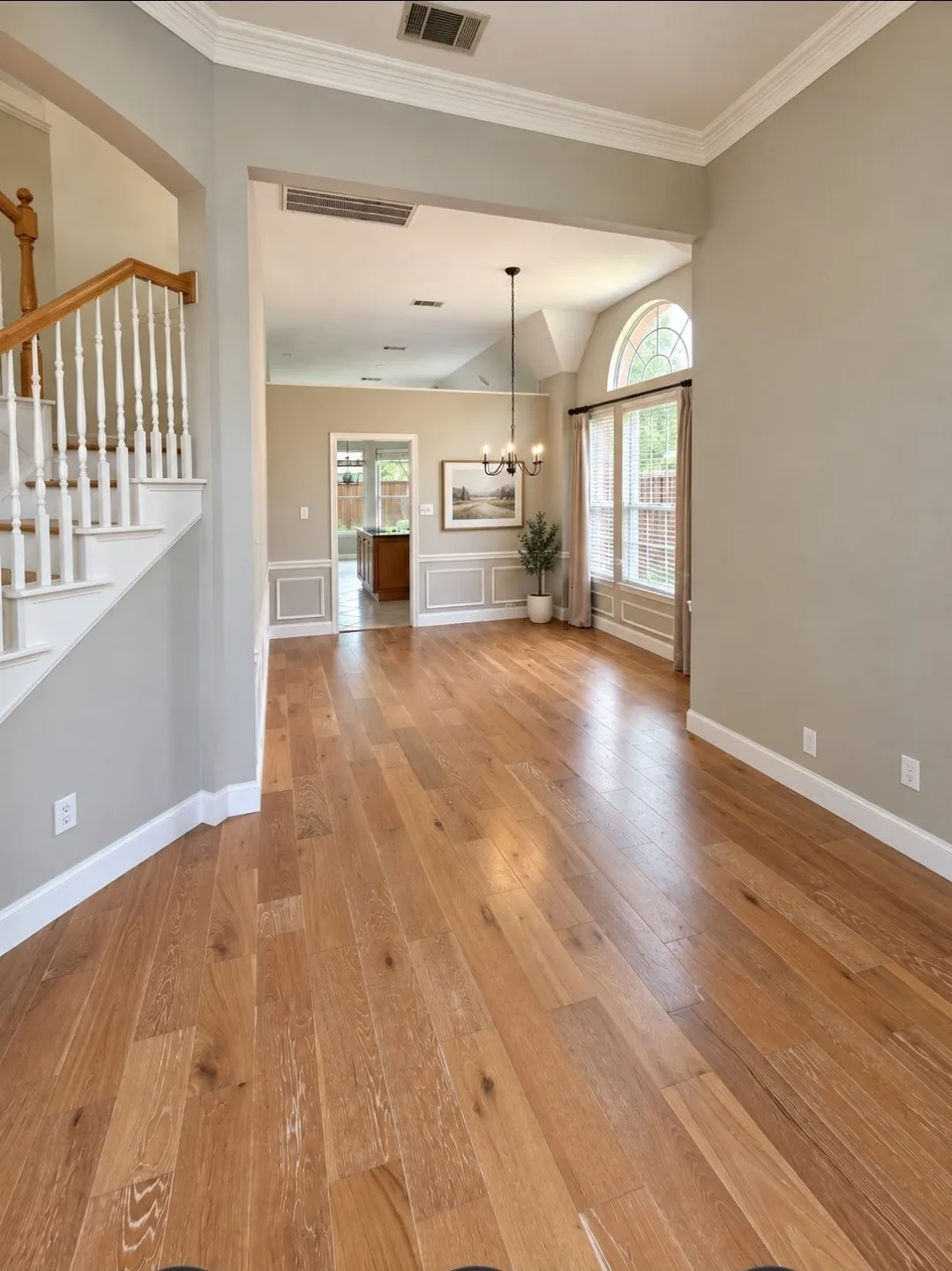 Wood-finish flooring throughout, white crown molding, and a vaulted ceiling with an arched window