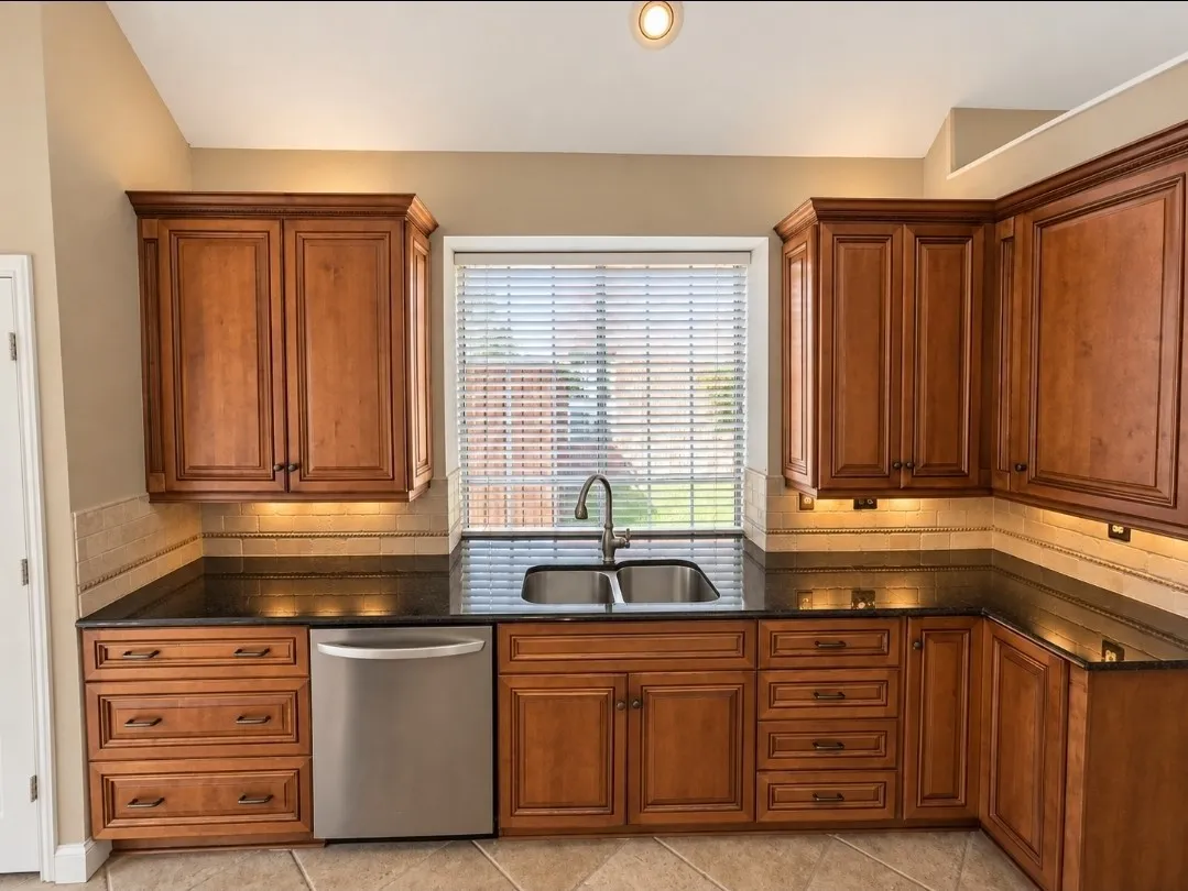 Kitchen featuring wood cabinetry, dark countertops, tiled backsplash, and stainless steel dishwasher