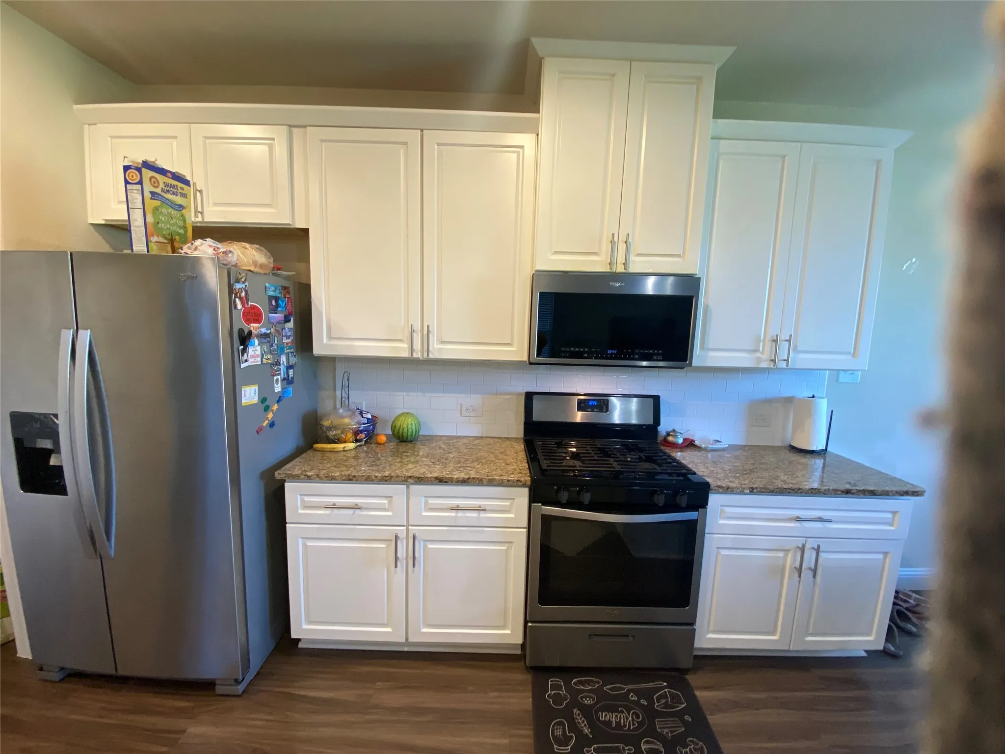 Kitchen with appliances with stainless steel finishes, decorative backsplash, dark wood-style floors, and white cabinets
