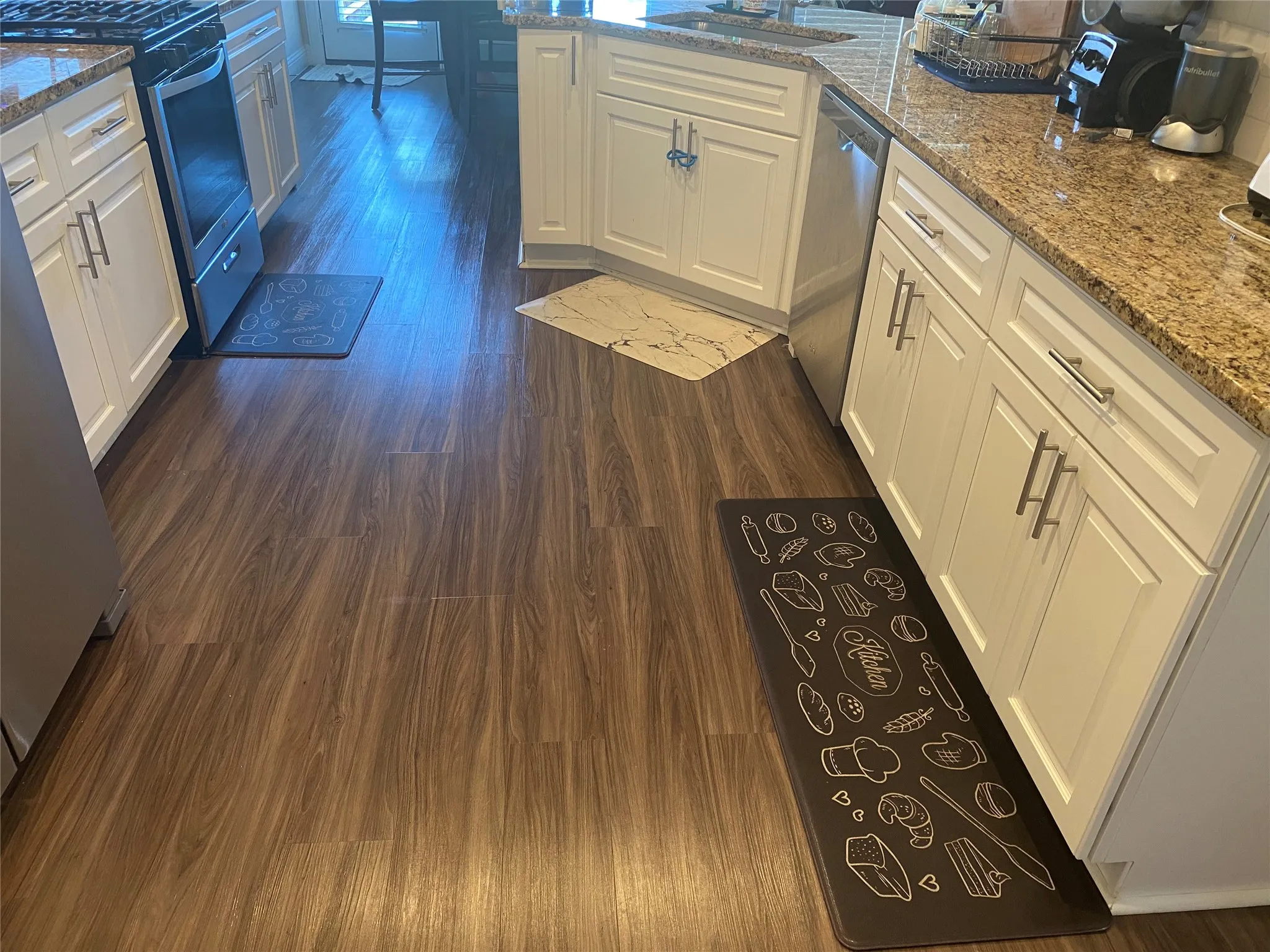 Kitchen featuring dark wood-type flooring, appliances with stainless steel finishes, white cabinetry, and light stone countertops