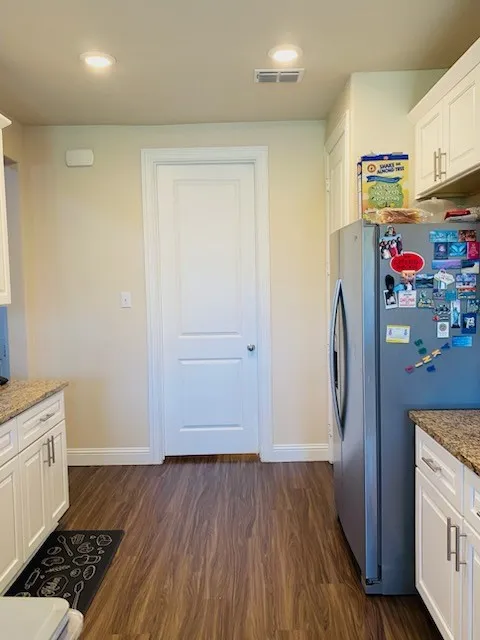 Kitchen featuring freestanding refrigerator, dark wood-type flooring, light stone counters, white cabinets, and recessed lighting