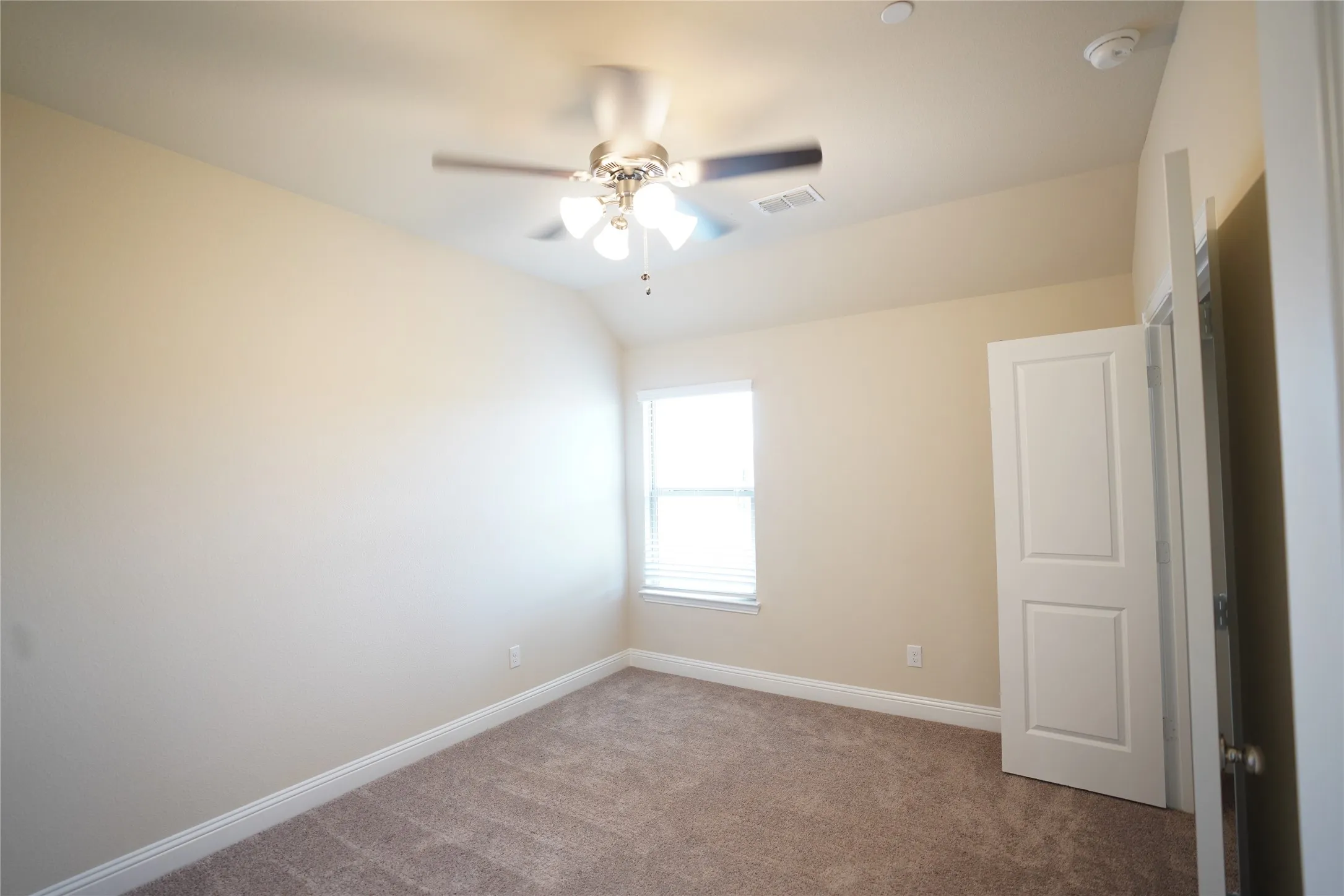 Carpeted empty room featuring ceiling fan, vaulted ceiling, and a smoke detector