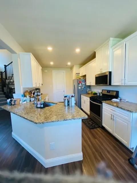 Kitchen featuring appliances with stainless steel finishes, dark wood finished floors, white cabinets, light stone counters, and a peninsula