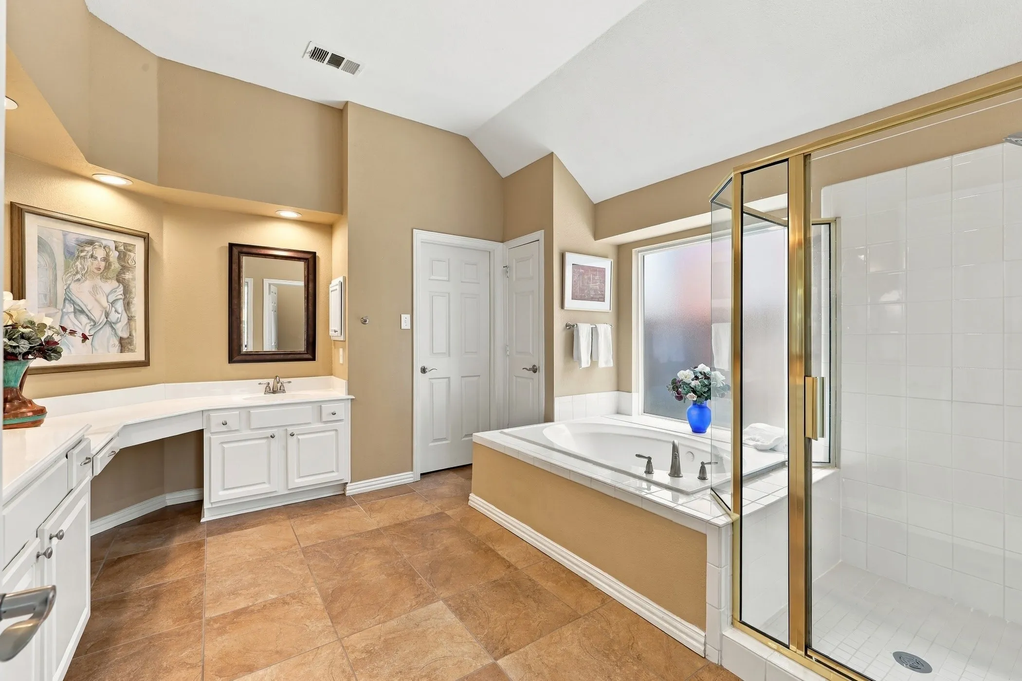 Generous soaking tub, separate glass-enclosed shower, dual vanity with built-in cabinetry, tiled flooring, and vaulted ceiling