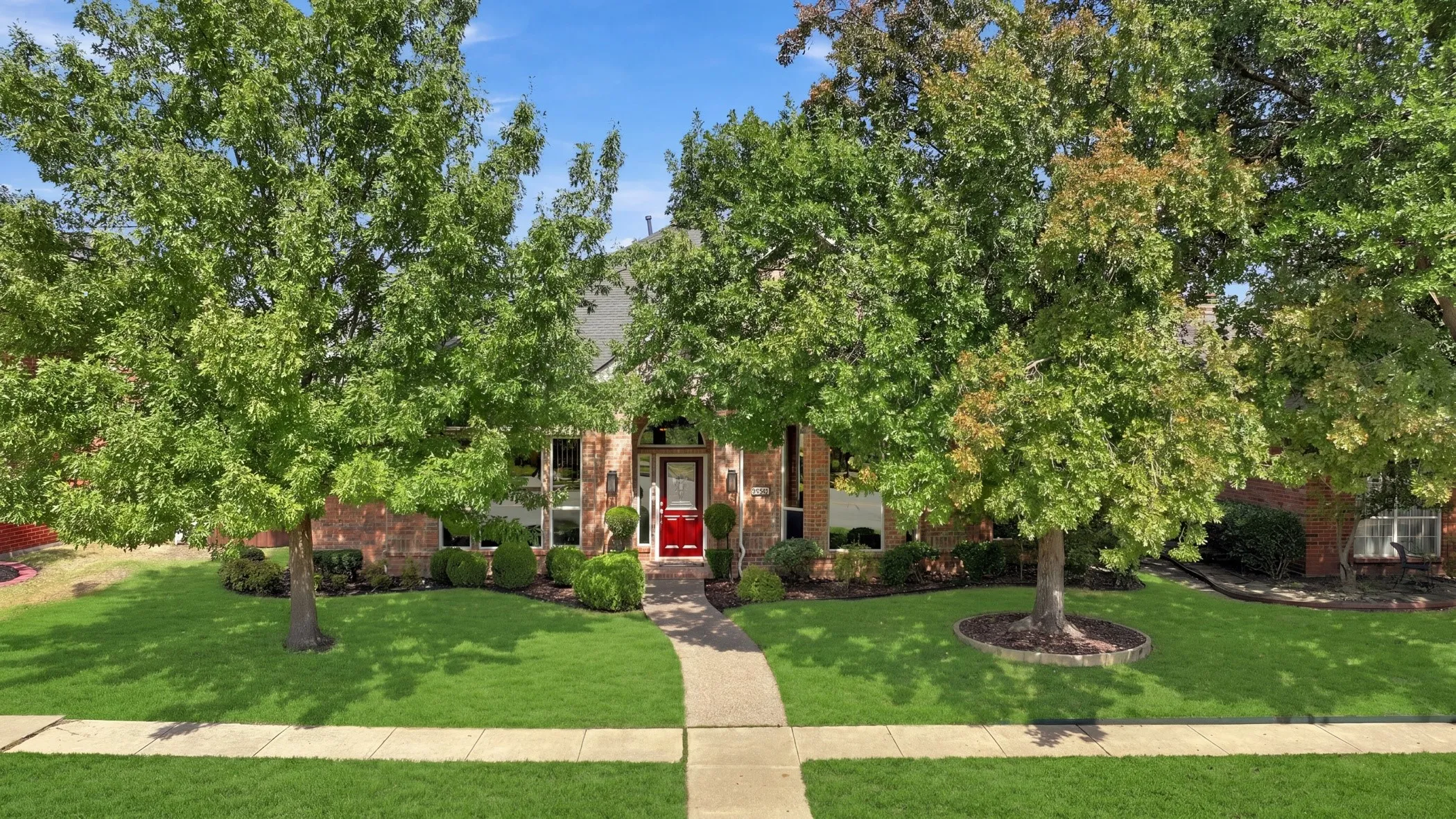 Brick exterior with a vibrant red front door, framed by mature trees.